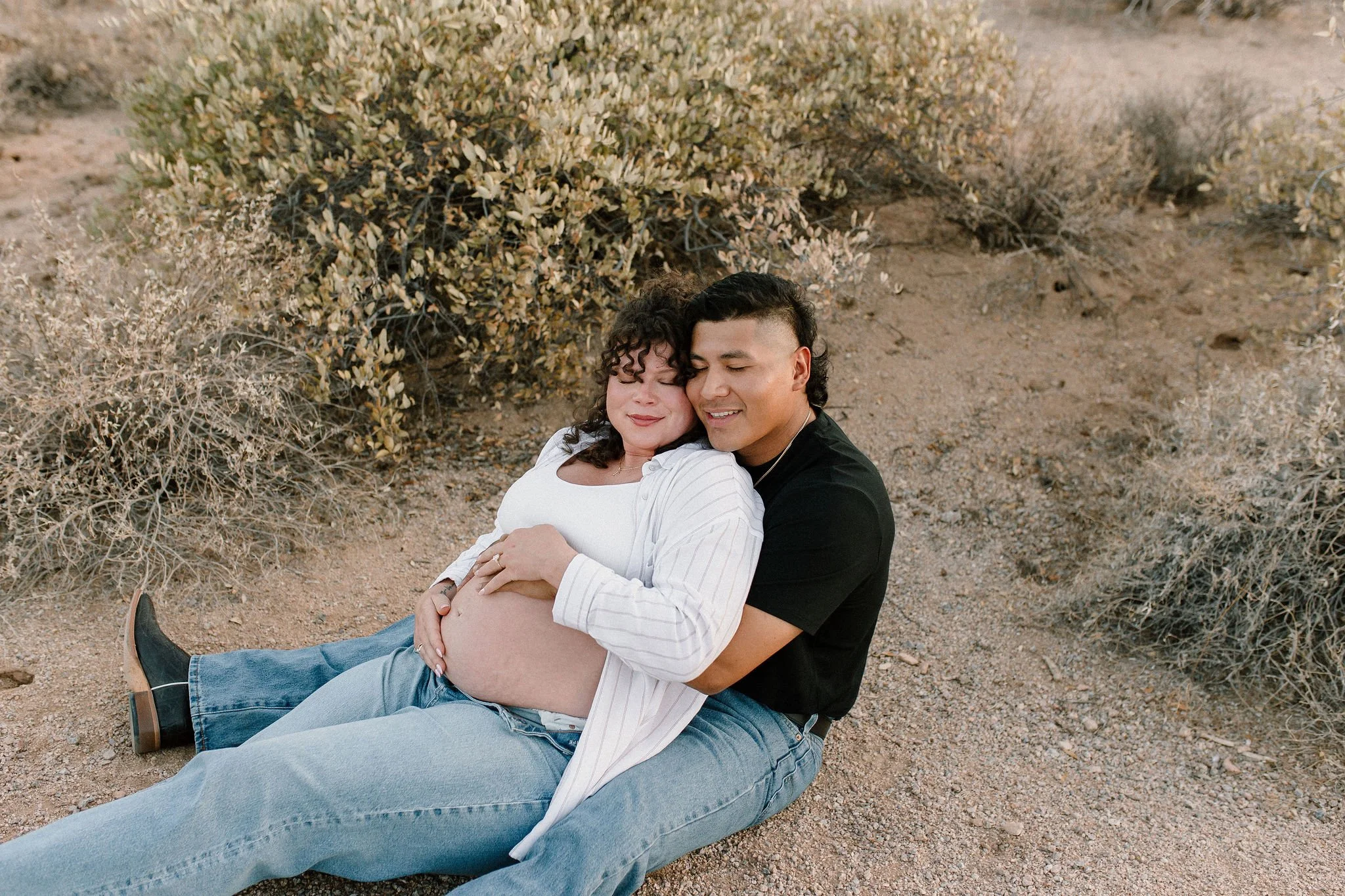 pregnant mom and dad sitting holding baby belly in desert Gilbert Arizona maternity photoshoot