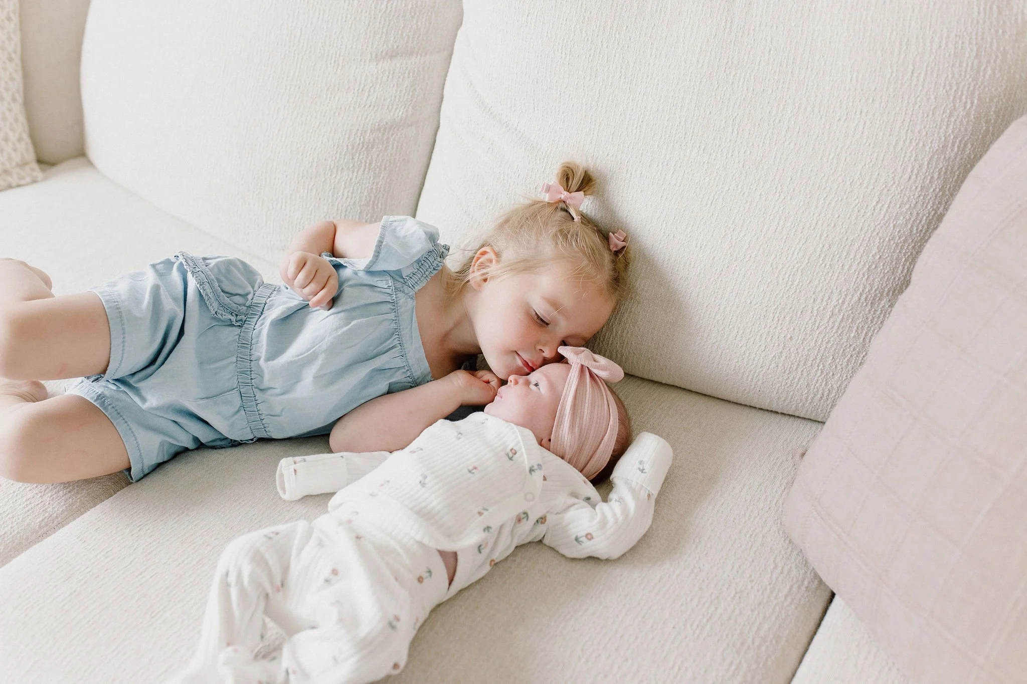 newborn photographer captures big sister kissing newborn baby sister in lifestyle newborn photography session