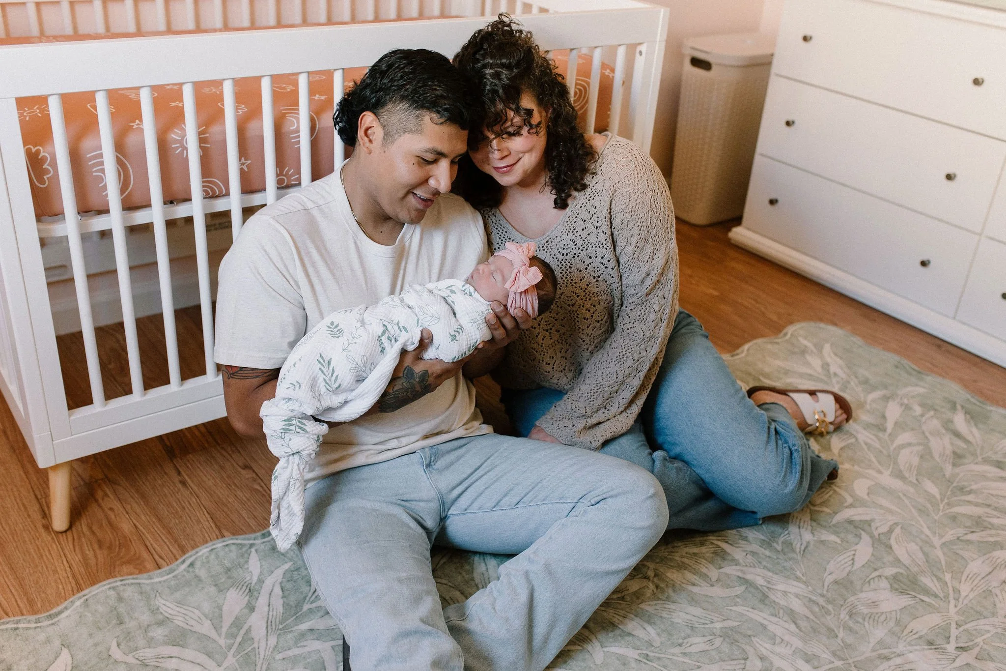 mom and dad sitting in nursery against the crib holding baby  in-home newborn photography session in Gilbert, AZ