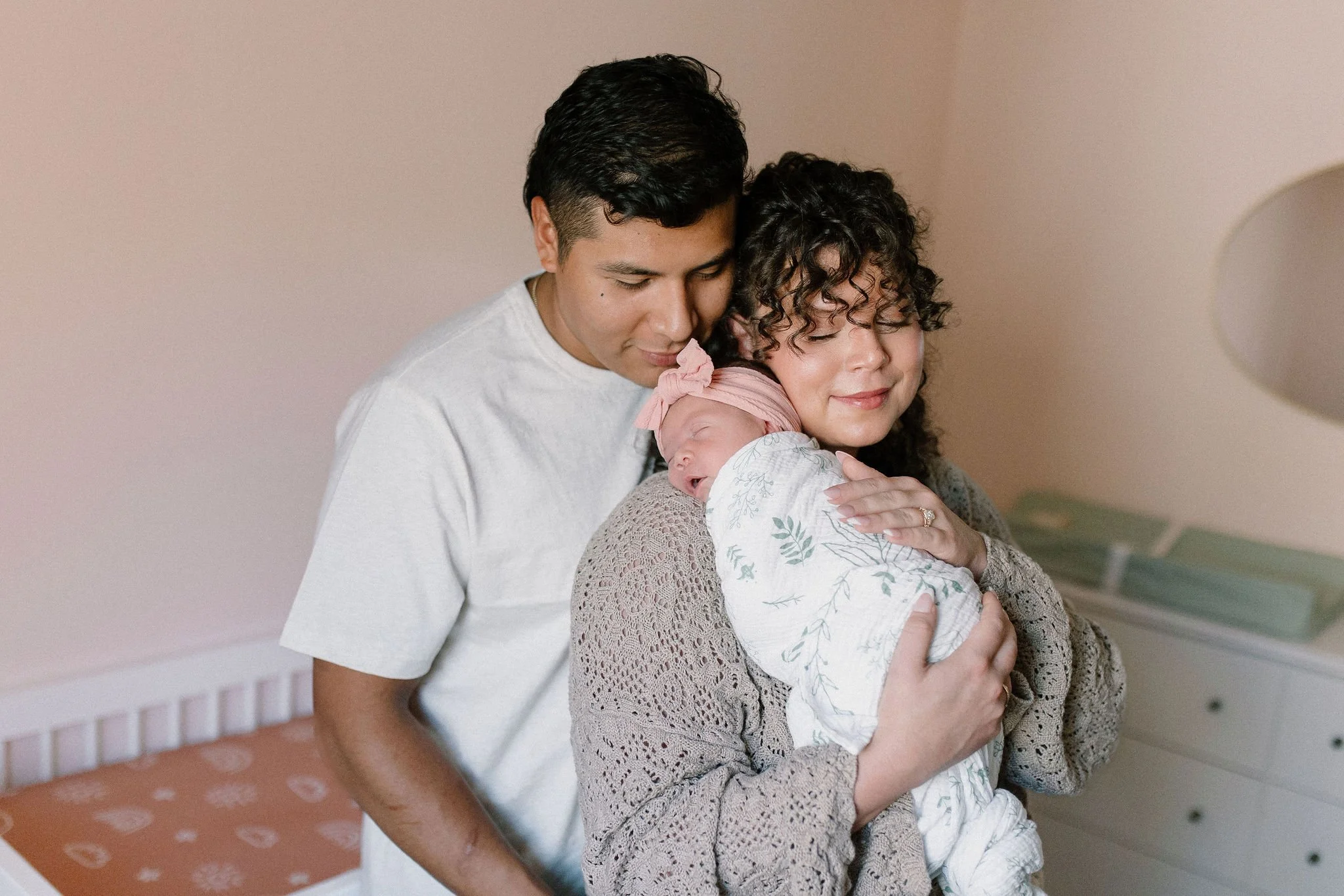 newborn baby laying on mom shoulder dad hugging both in baby nursery