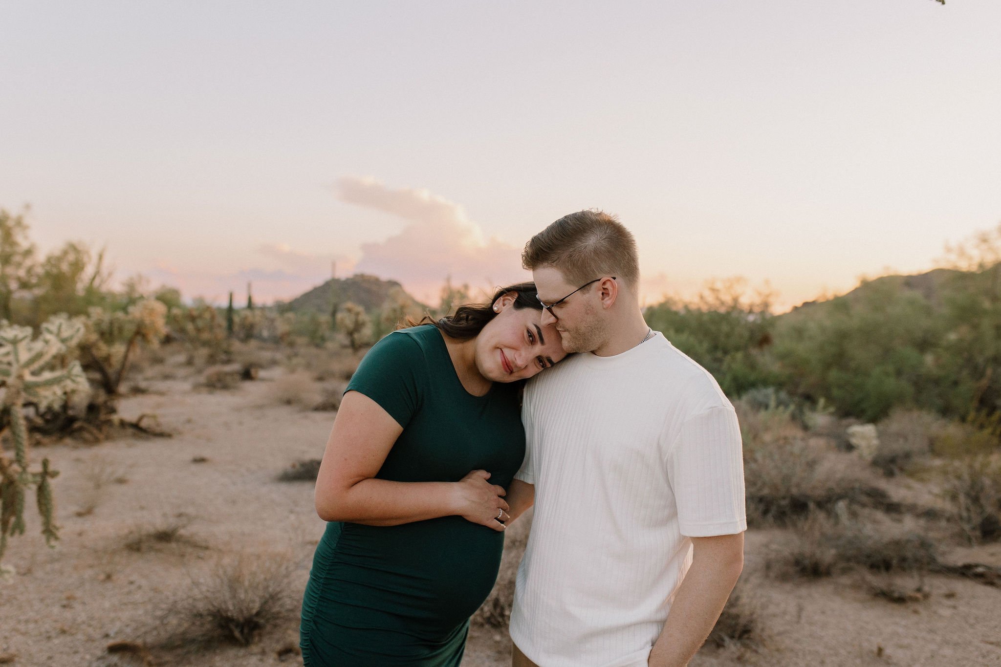 pregnant mom holding belly laying her head on her husband in Gilbert Arizona desert in maternity photography session