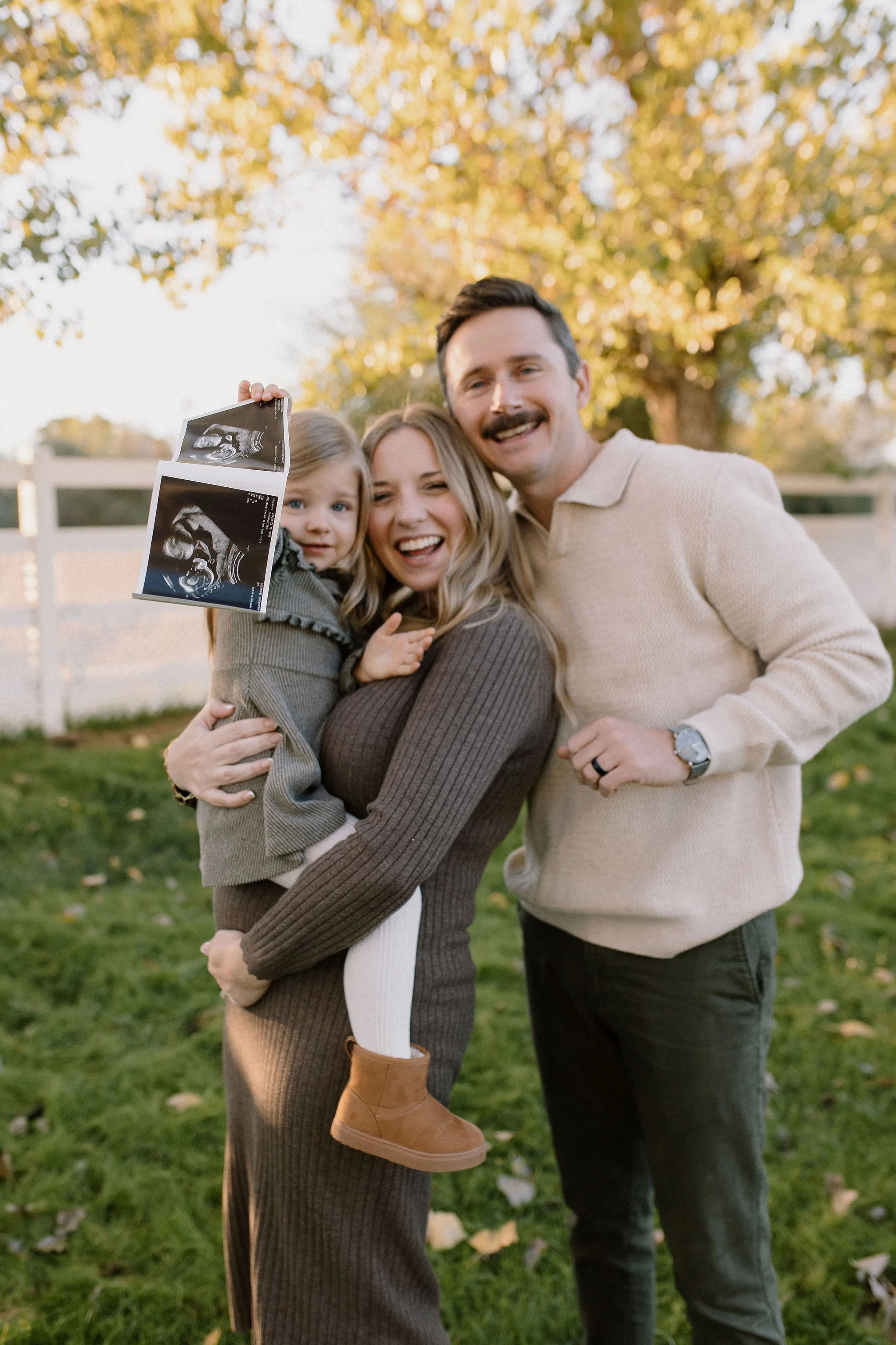 pregnant mom holding toddler and belly with dad and ultrasound picture in mesa farm maternity photo session