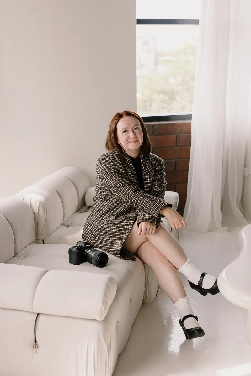 photographer sitting on couch with camera sitting next to her in neutral studio in Gilbert, Arizona