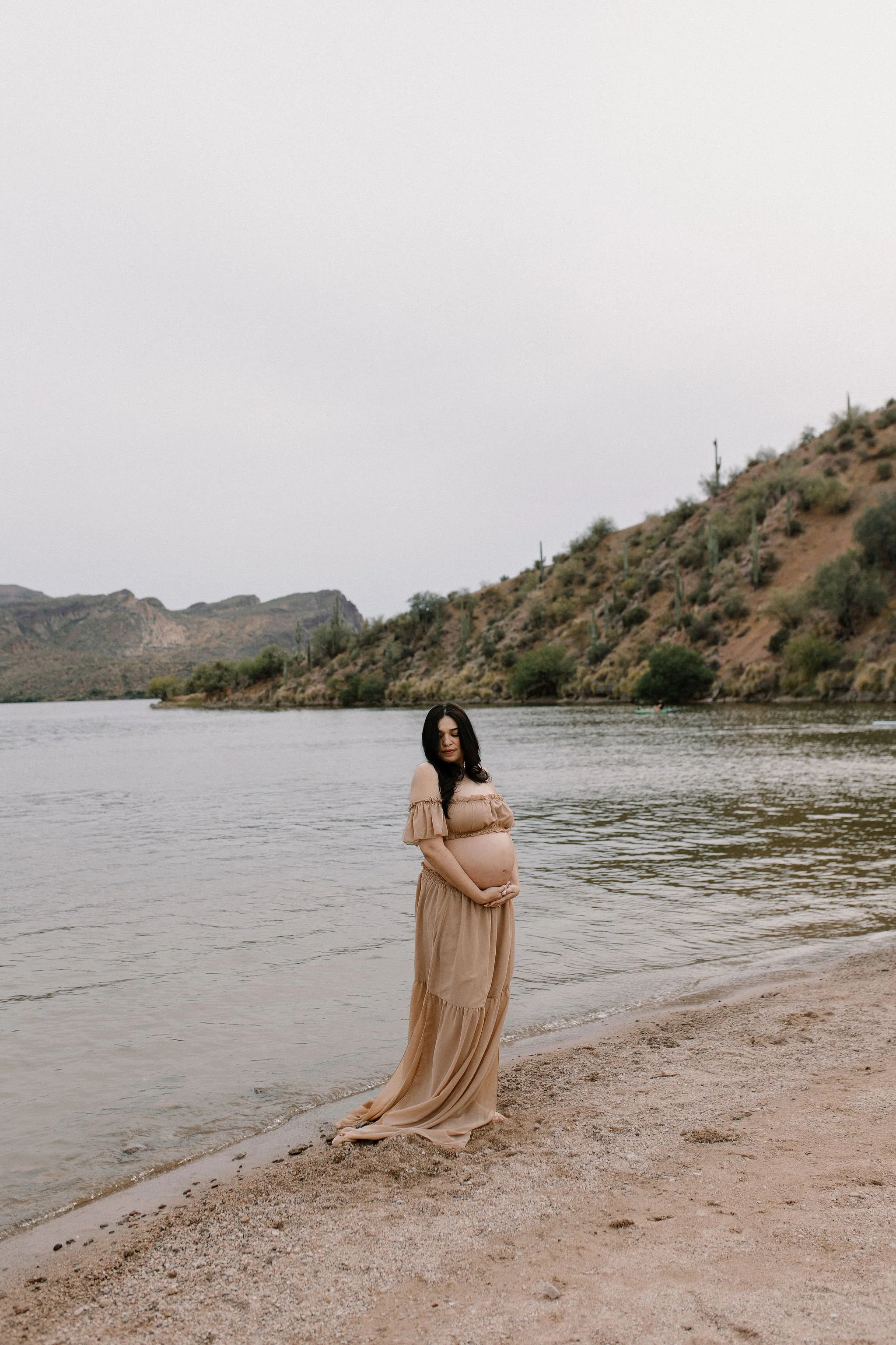 pregnant mom holding belly in Arizona desert lake by Mesa maternity photographer