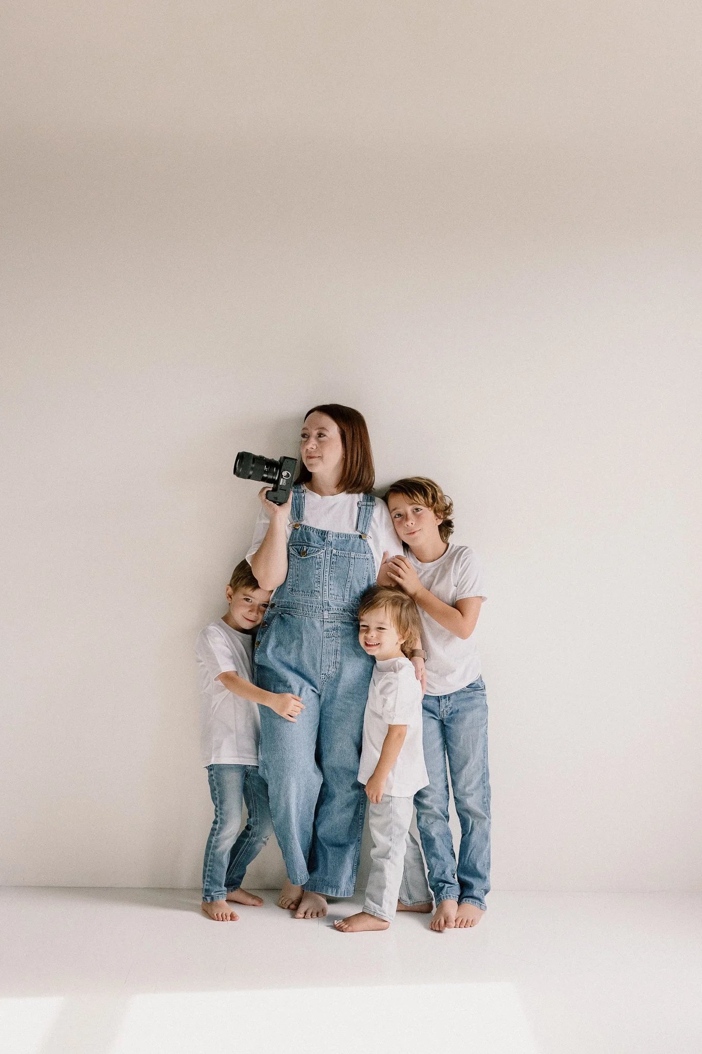 family photographer standing with her kids in a neutral studio space in white shirts and jeans