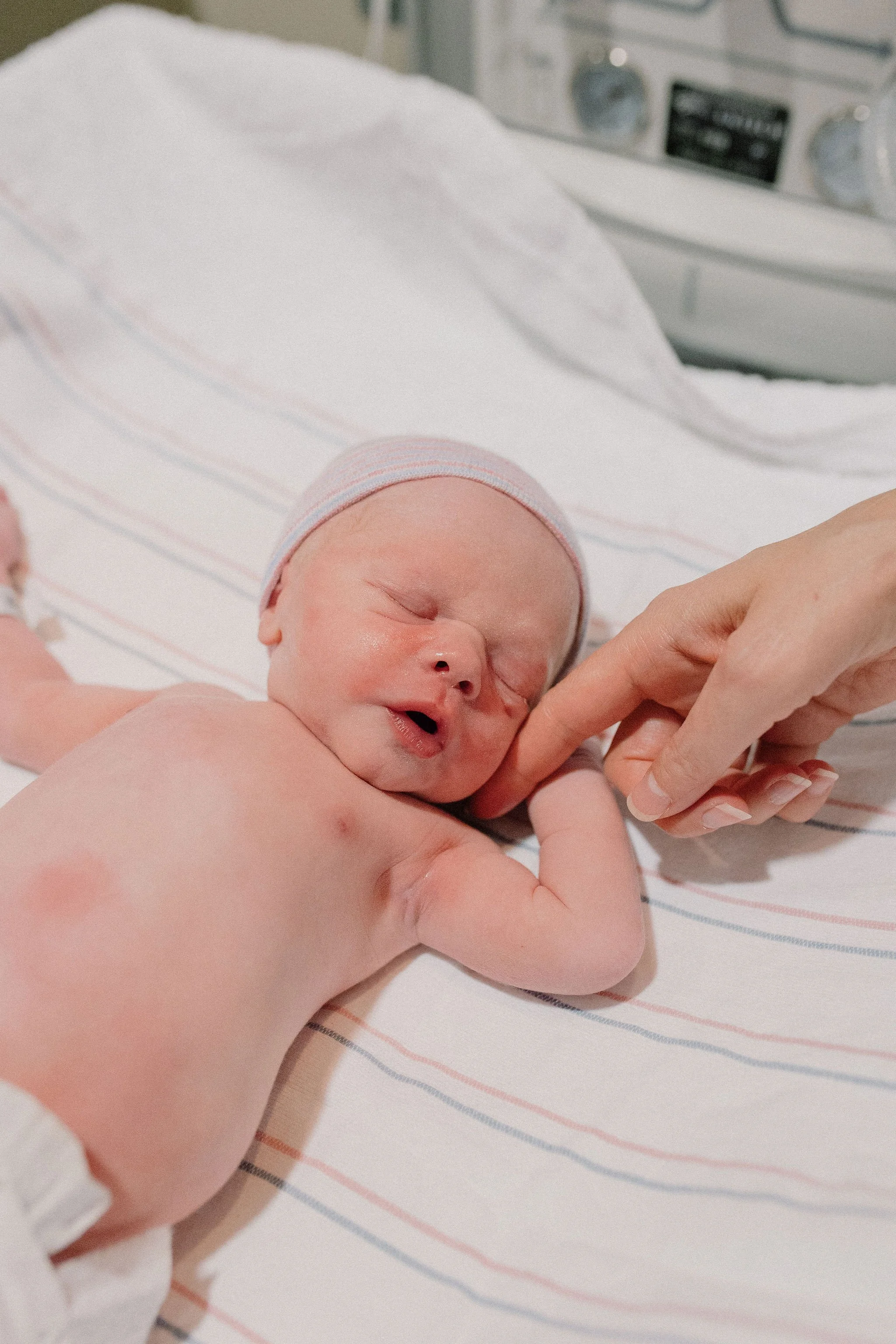 newborn baby holds mom's finger in the warmer at the hospital immediately after birth