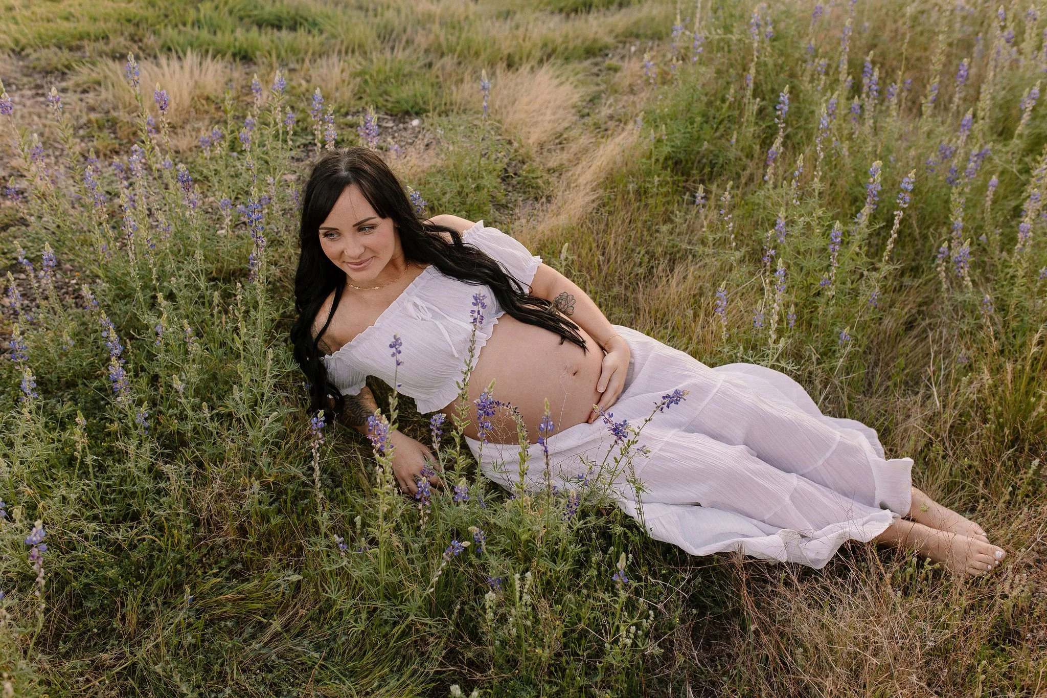 pregnant mom laying in wildflowers holding belly in desert maternity photoshoot in Gilbert AZ