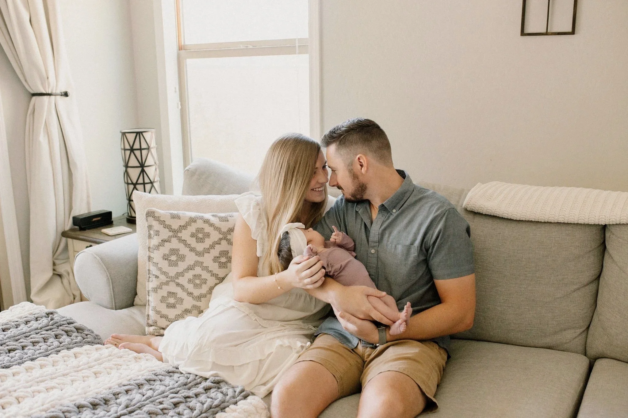 mom and dad looking at each other while holding baby in living room by Mesa newborn photographer