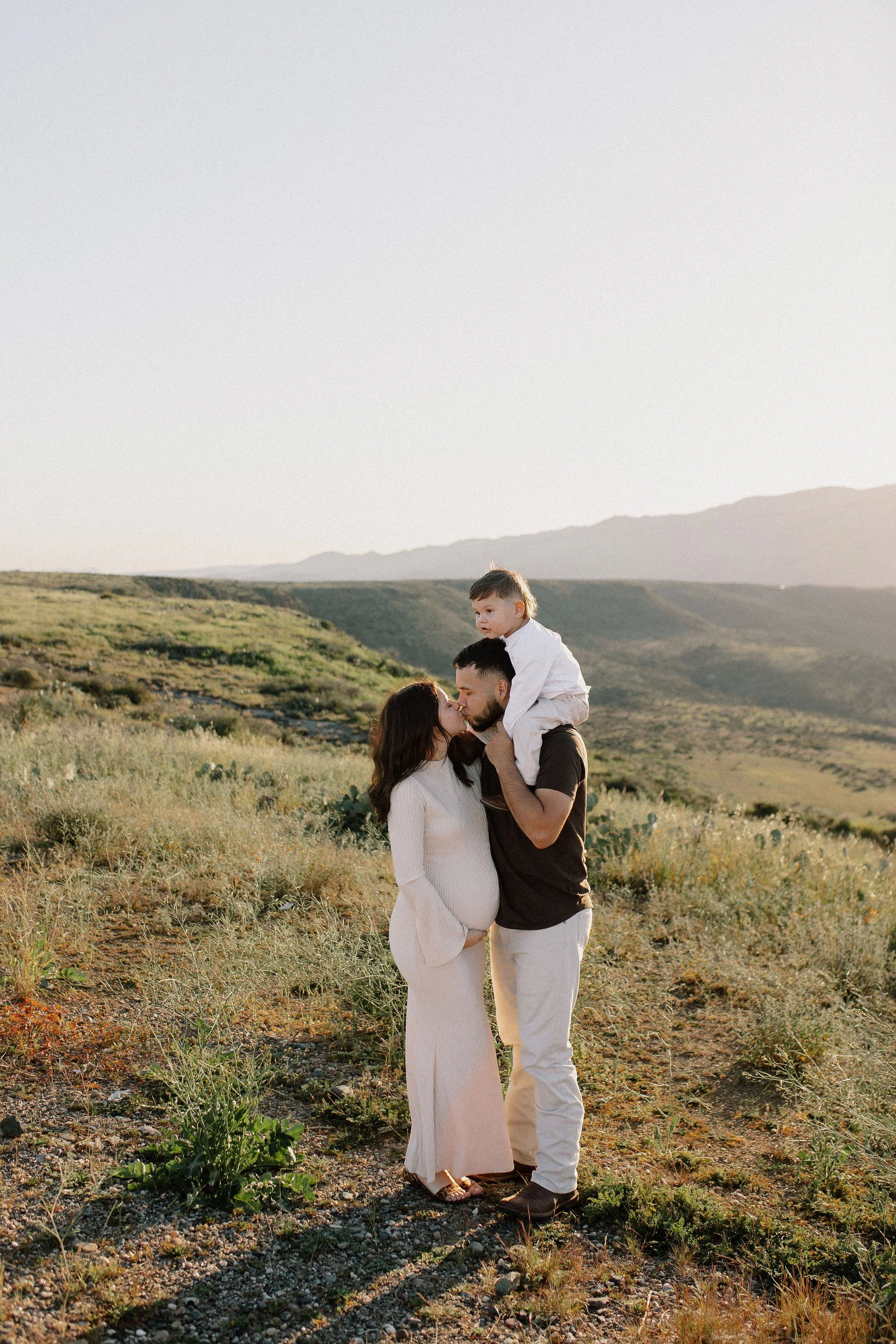 pregnant mom kissing dad with toddler on shoulder in Sunset Point Phoenix maternity photo session