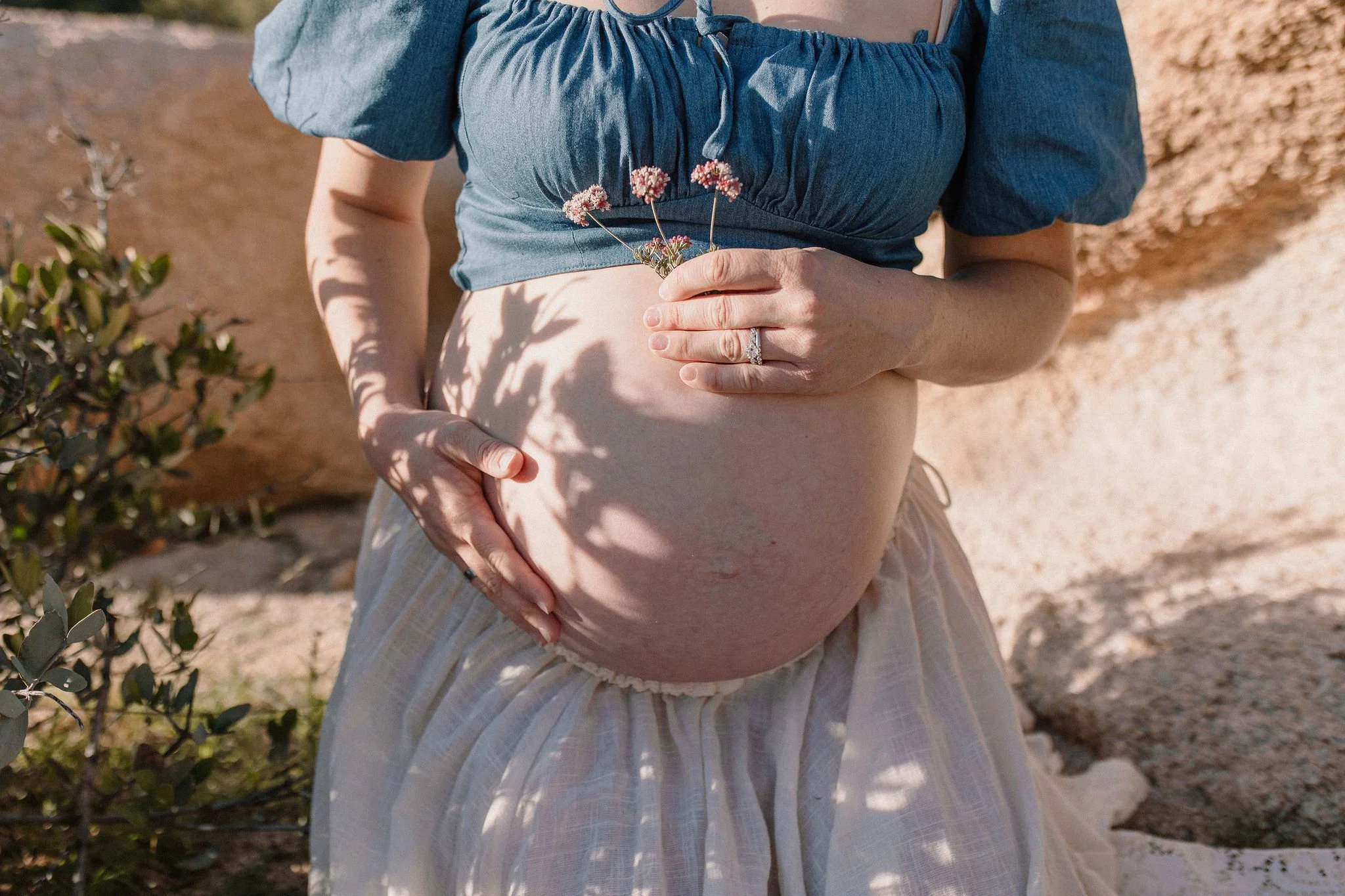 Pregnant belly detail photo with flowers and artistic shadows in desert maternity session