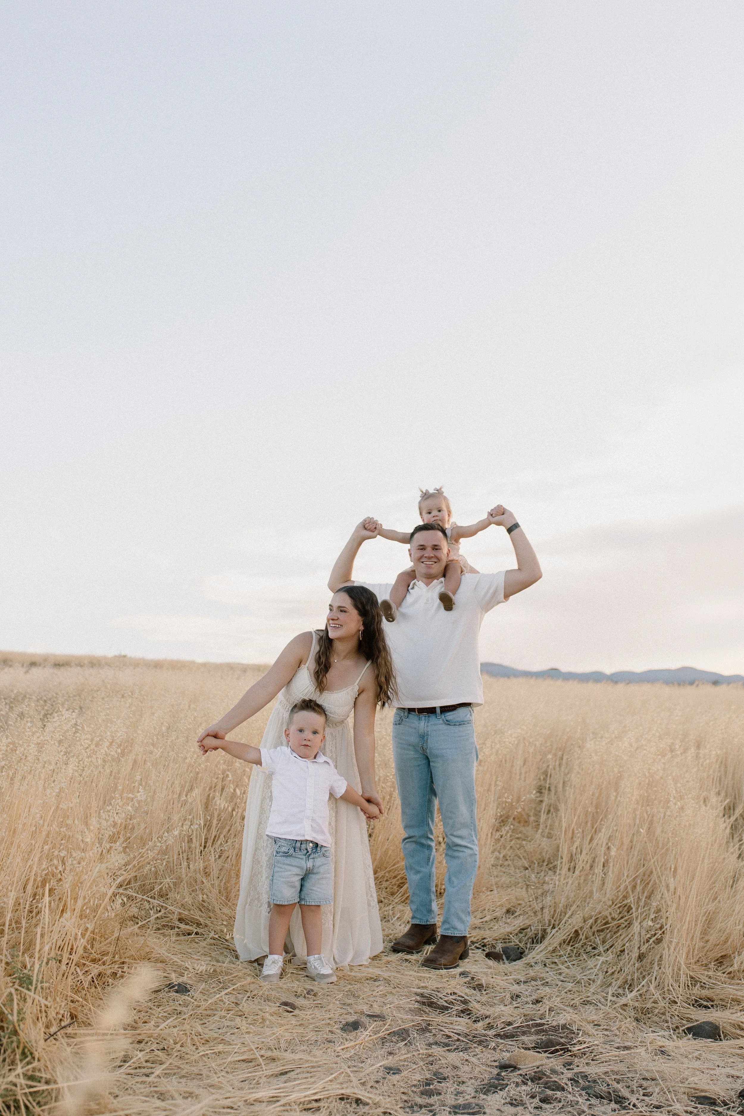 family standing together pretending to be airplanes in tall yellow grass field