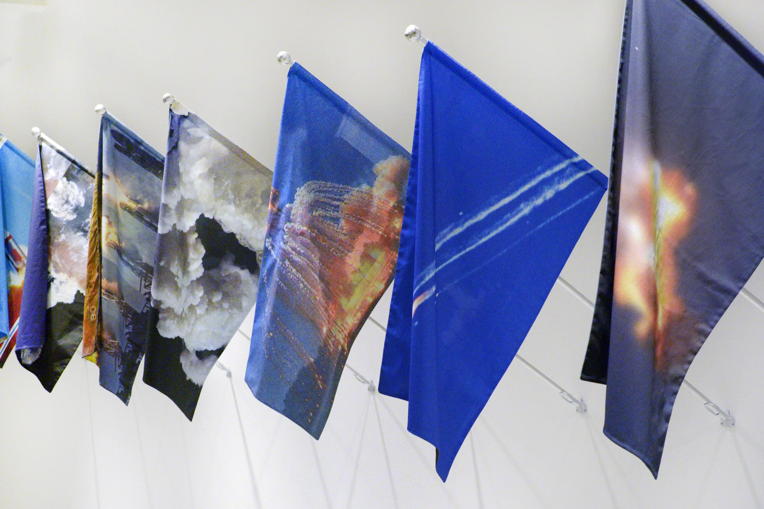 Installation view: T-Minus Ø , 2017. Installation of 13 mounted flags. Digital print on cotton with aluminum pole, artist-made finial, zinc pole mount. Flag: 24 x 36" pole: 73 x 1/2 x 1/2" 