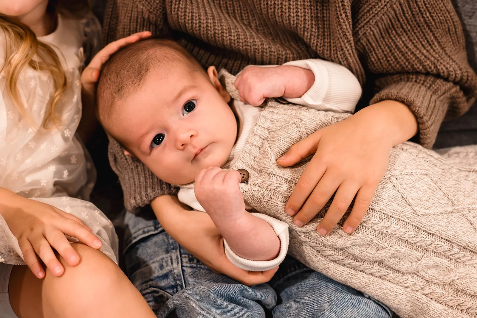 Family sitting on a bed with a newborn baby. The father leans over, and the mother holds the sleeping baby, while a young girl sits nearby snuggling dad.