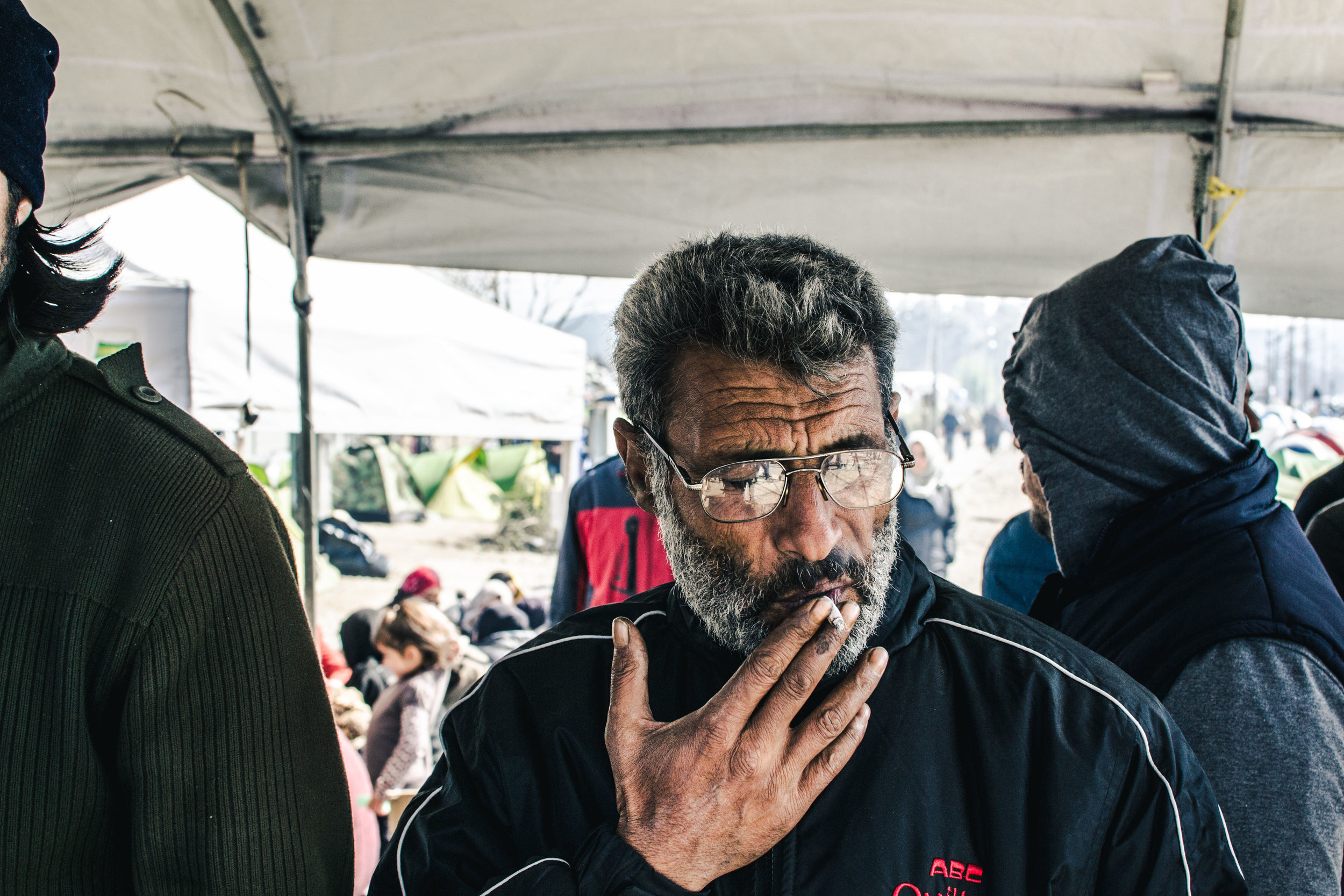 An Afghan refugee drags on a cigarette under a large awning, where groups of migrants would sing songs from times of the revolution in the 70s.