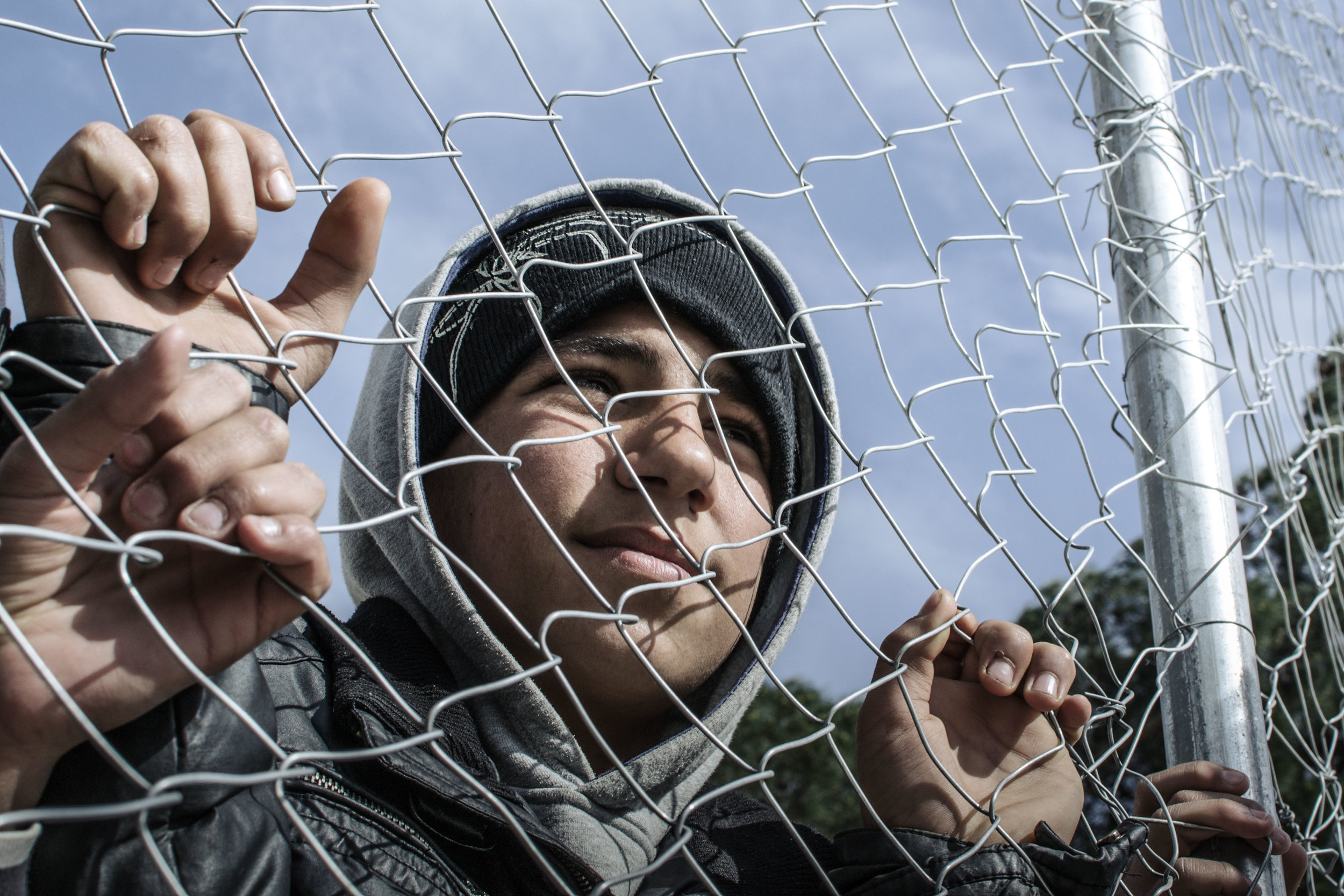 Amir, 12, looks through the wire fencing that surrounds Diavata refugee camp. The compound was originally used by the Greek army, but was been inundated by families of refugees who had been assigned there by the government. In nearby Thessaloniki, p