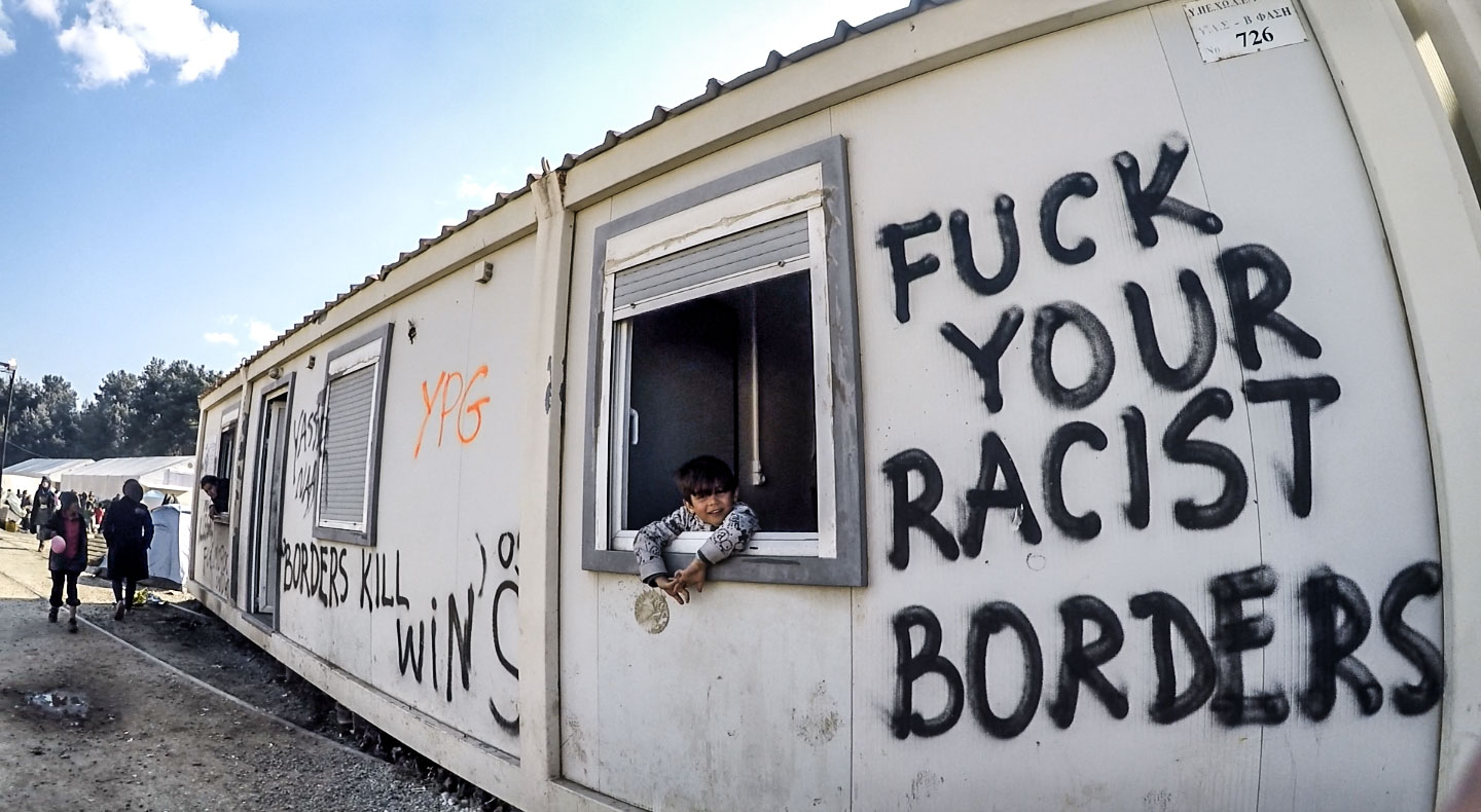 A young boy smiles, hanging out of the window of his family's graffitied cabin in Eidomeni camp. Rising tensions in the camp led to riots, where Greek police fired canisters of tear gas into crowds. Days before I arrived at the camp, two individual