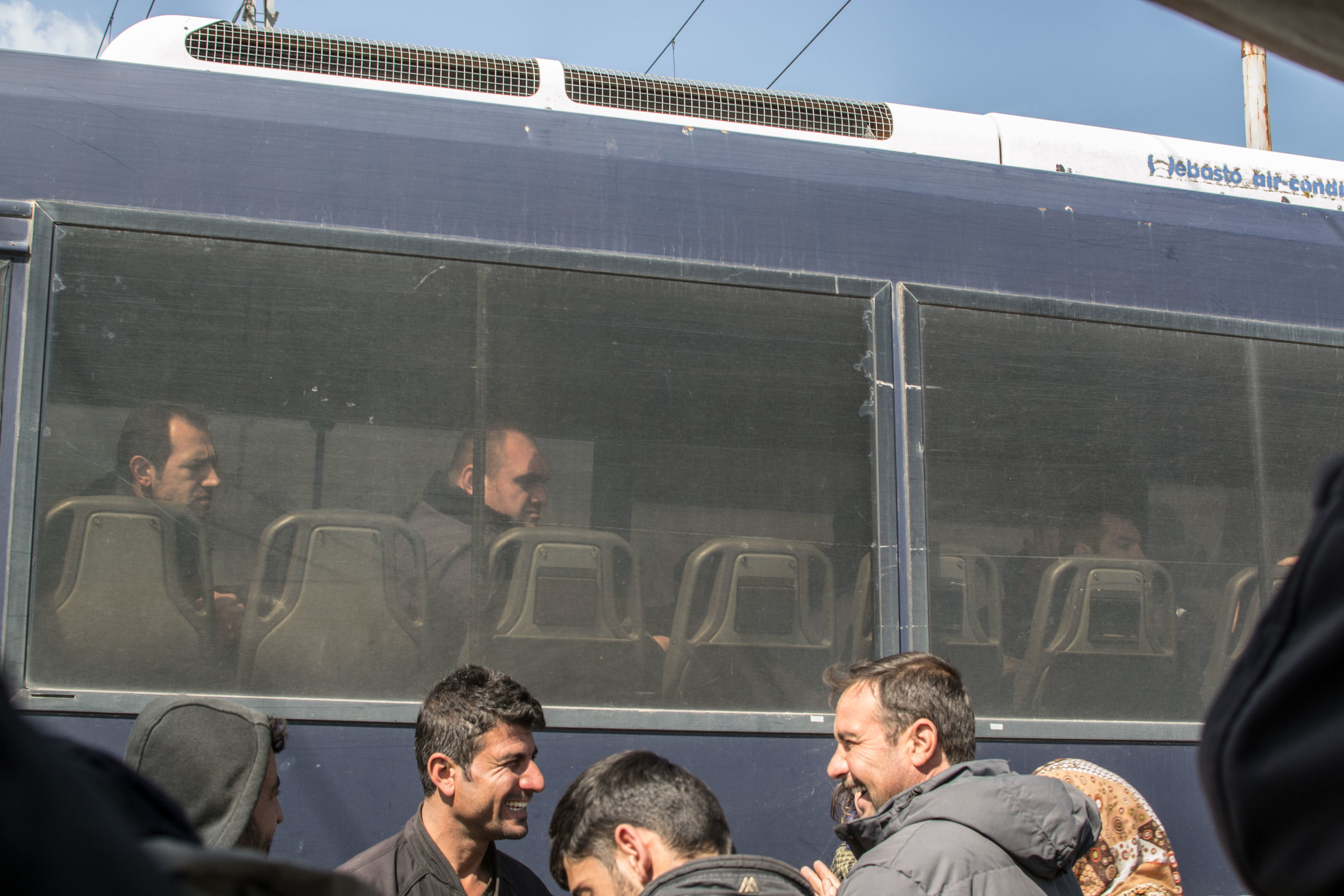 Greek police grimace at smiling refugees from their bus, which was blocking the train tracks from Greece into Macedonia.