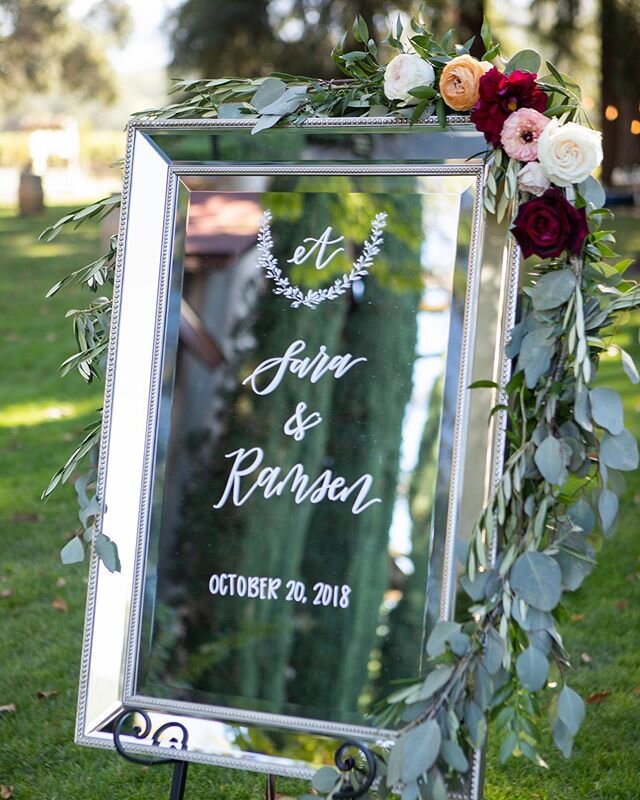 A hand calligraphed mirror with lush floral decorations is a stylish way to welcome guests to an outdoor ceremony. As seen on @tacariweddings .
.
.
Planning &amp; Design: @alafrancaiseevents 
Photography: @wasio 
Venue: @charleskrugweddings 
Floral: 