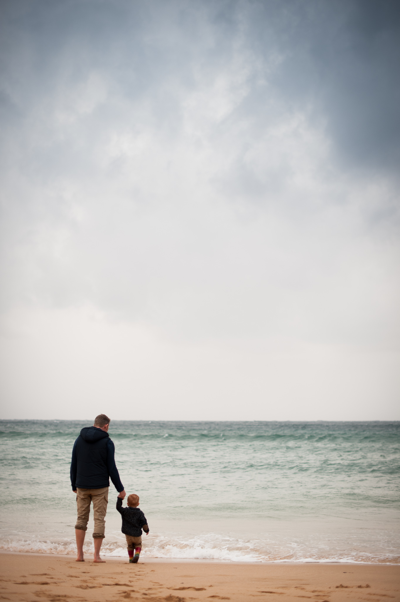 Father and son holding hands watching the waves