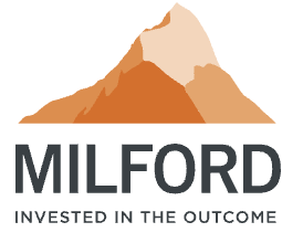 A beige ceramic vase with a narrow opening, holding a single dried floral stem, sitting on a wooden surface with sunlight creating shadows in the background.