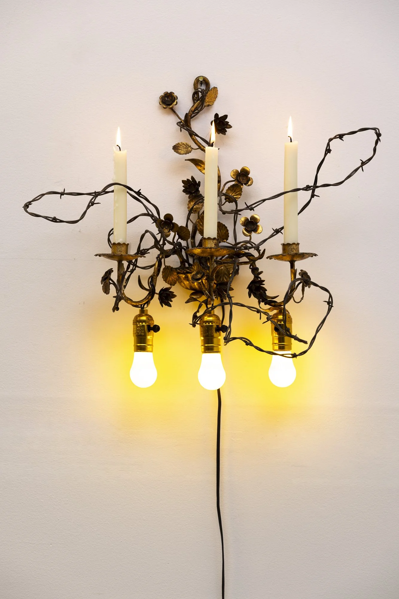  As Above So Below, 2026, 20 × 23 × 16 inches, antique candelabra, barbed wire, candles, electrical wire, yellow light bulbs.  