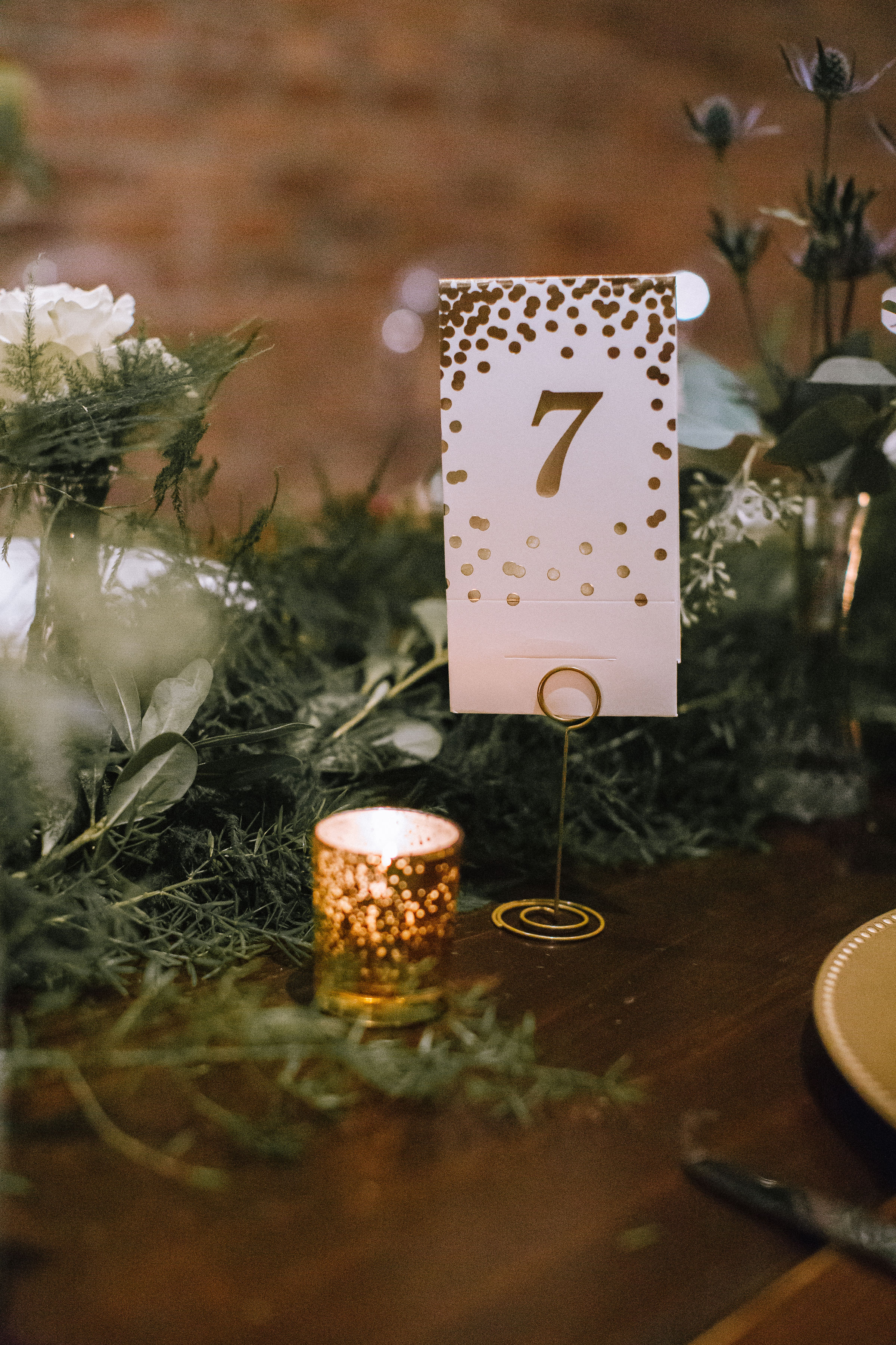 Gold wedding table numbers placed on wedding table with greenery and candles for Pittsburgh wedding at Studio Slate planned by Exhale Events. Find more wedding inspiration at exhale-events.com!