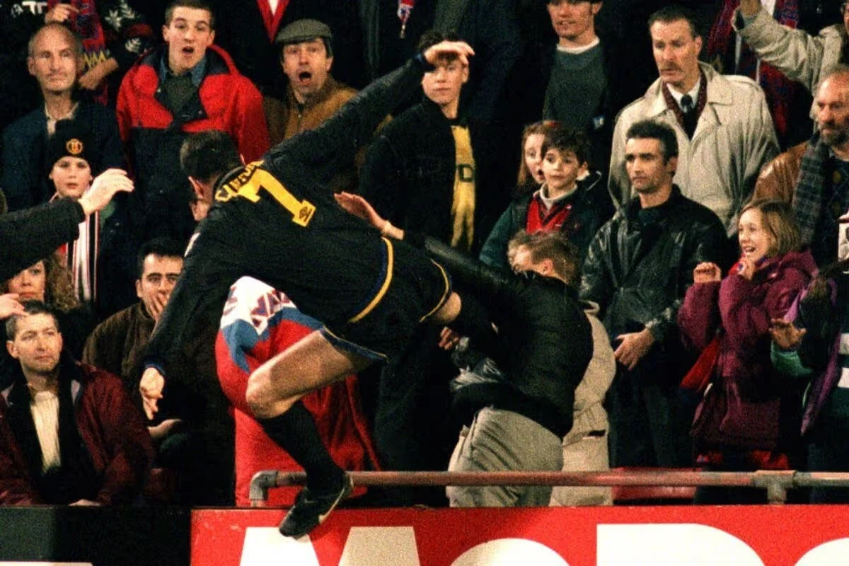 A photograph of Eric Cantona on the football pitch kicking a spectator, capturing a moment of aggressive action during a match.