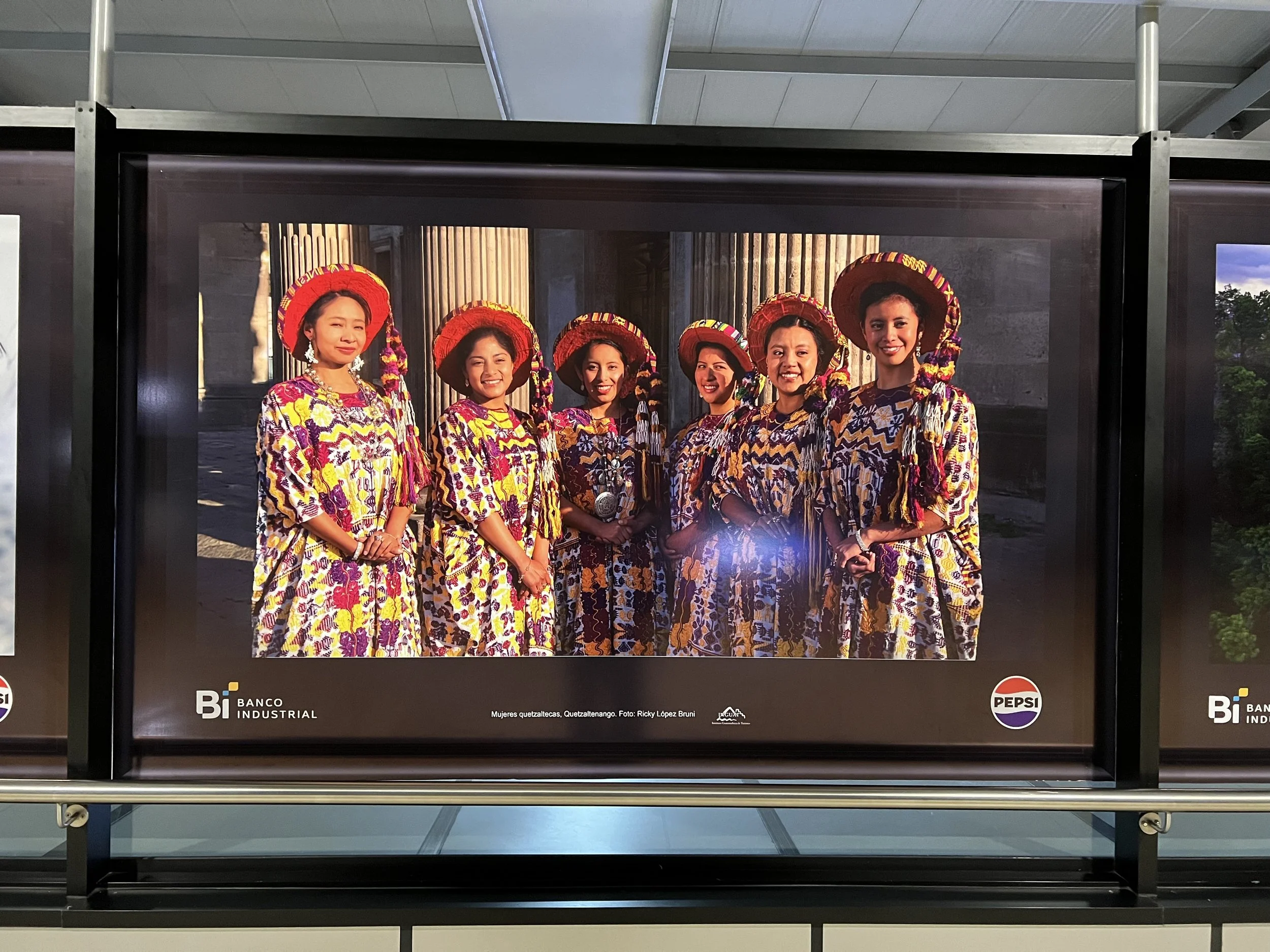 Posters in the arrival hall of Aurora International Airport with image of Indigenous women in traje from the region of Quetzaltenango.