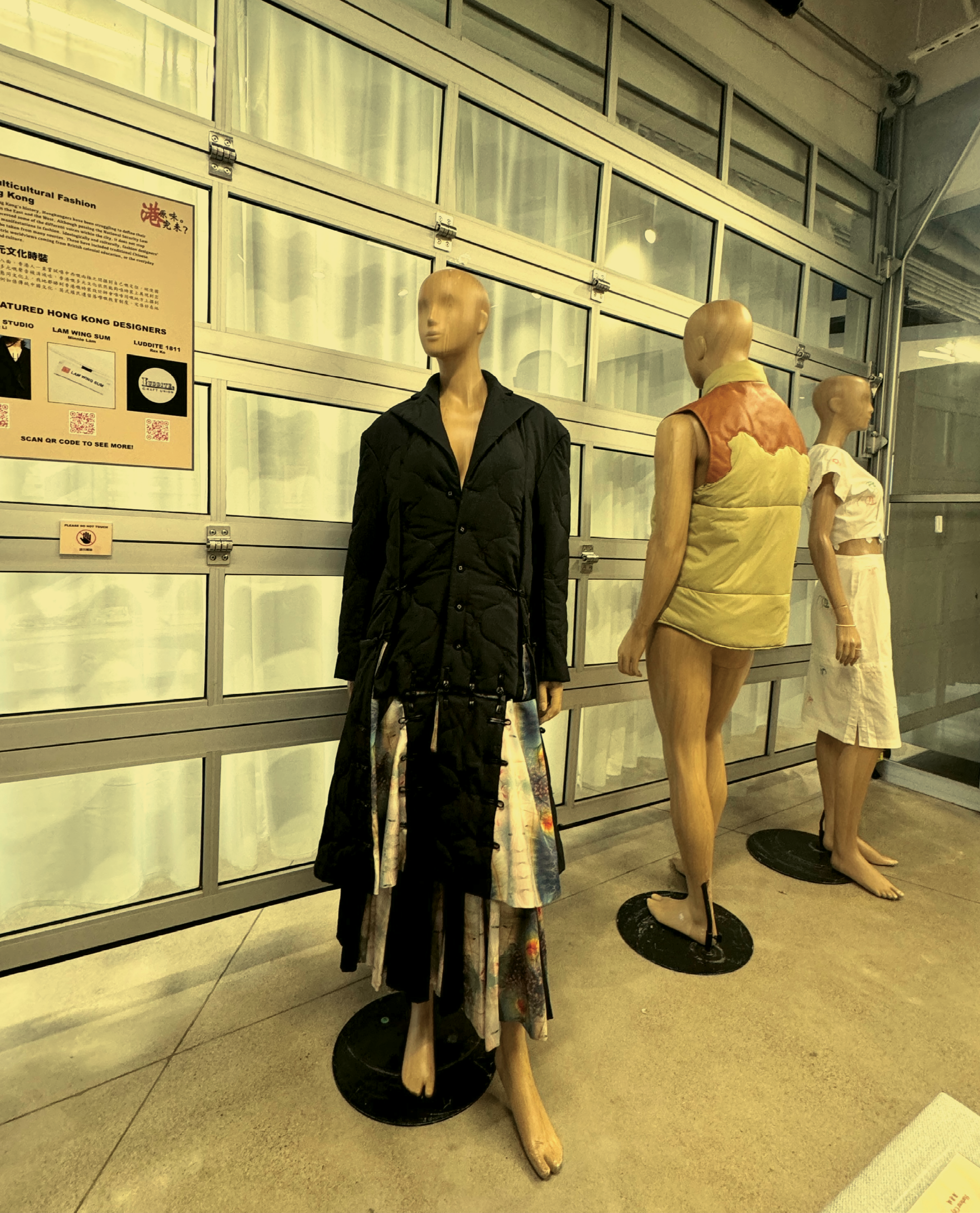 A photography showing the three displayed outfits in the exhibition. From left to right, they are Vincent Li Studio’s black ensemble, Luddite 1811’s vintage puffer vest, and Lam Wing Sum’s white dress.