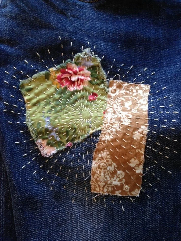 Sashiko mending on denim with visible white stitches on top of 2 patchworked fabric scraps.