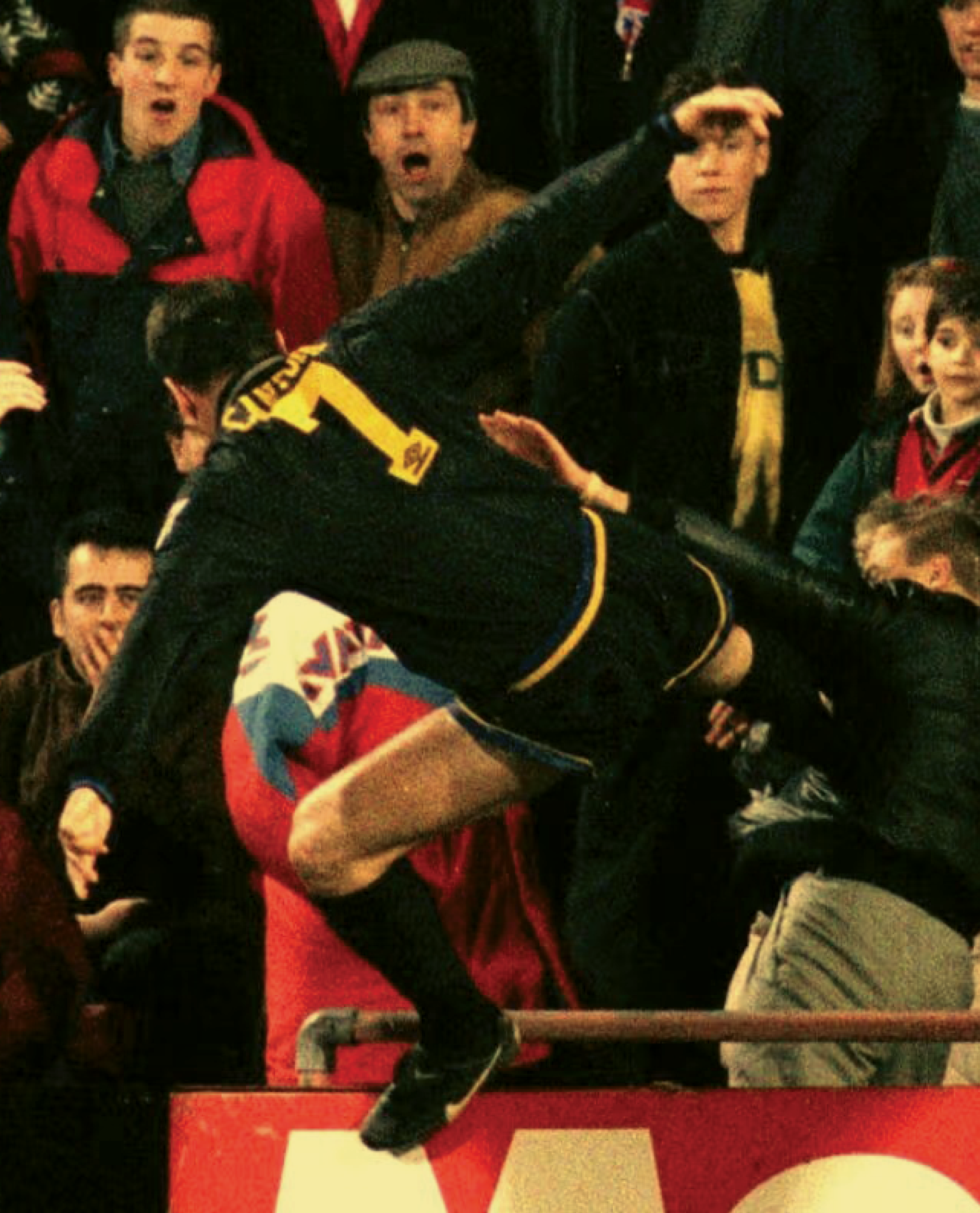 A photograph of Eric Cantona on the football pitch kicking a spectator, capturing a moment of aggressive action during a match.
