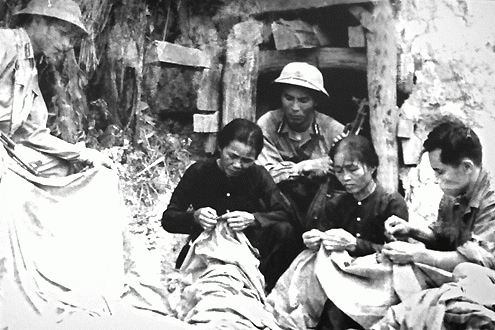 A black-and-white photo shows Mother Vien and Mother Diem mending a national flag on the bank of Hien Luong river. Revolutionary soldiers sit next to them.