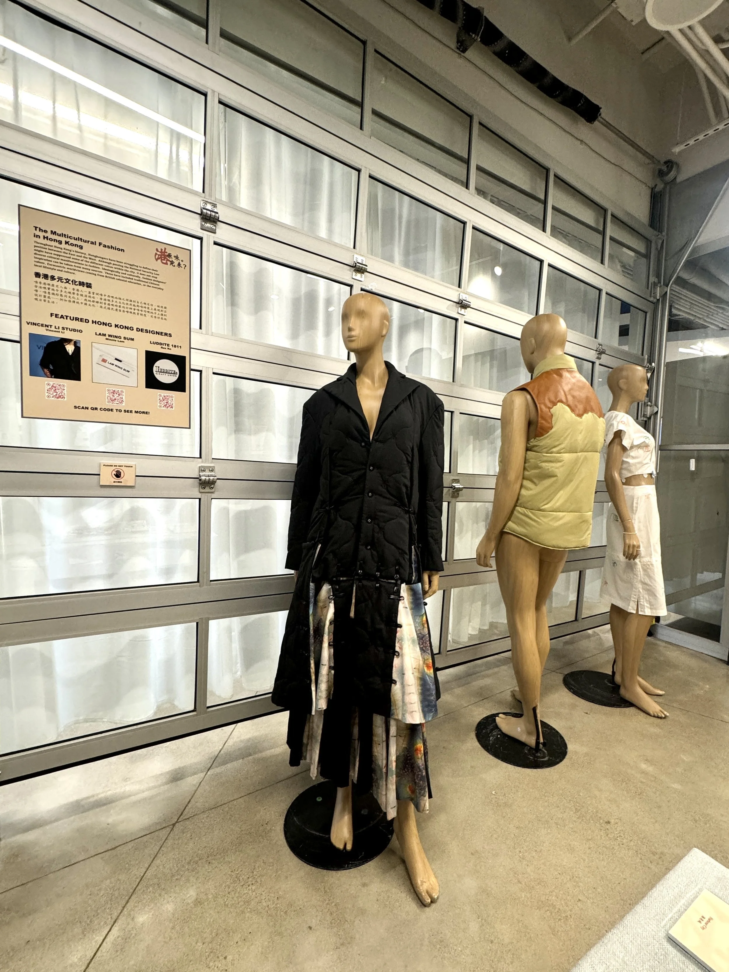 A photography showing the three displayed outfits in the exhibition. From left to right, they are Vincent Li Studio’s black ensemble, Luddite 1811’s vintage puffer vest, and Lam Wing Sum’s white dress.