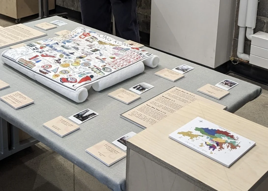 A semi-close-up photography showing the central display table, How Much Do You Know about Hong Kong?, from a ¾ angle. On the display table, there is an elevated exhibit of a square white handkerchief, accompanied by some polaroid images.
