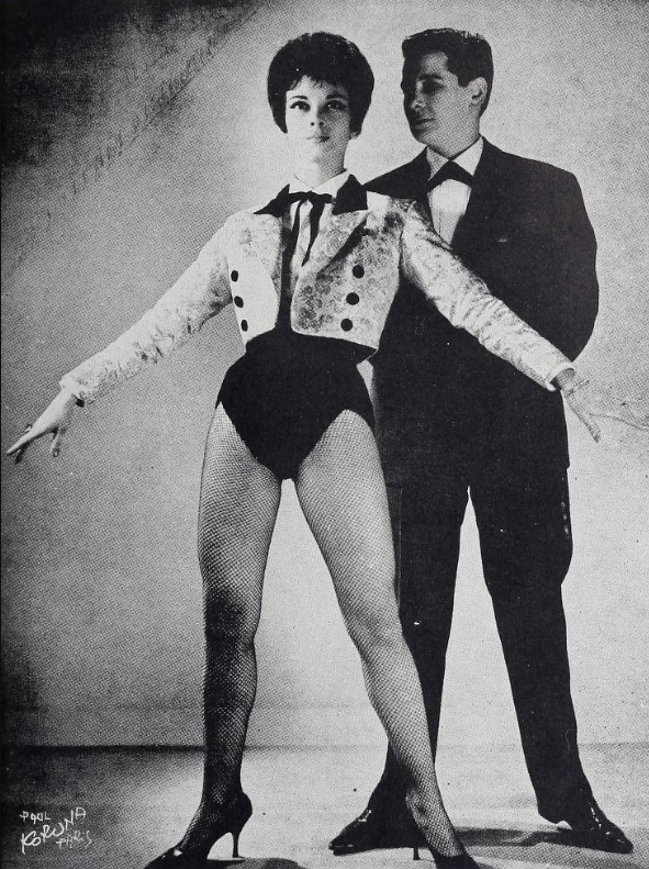 Maxime wearing tights, a bodysuit, and cropped fitted jacket standing in front of the male impersonator Jacky who wears a full suit and small tie.