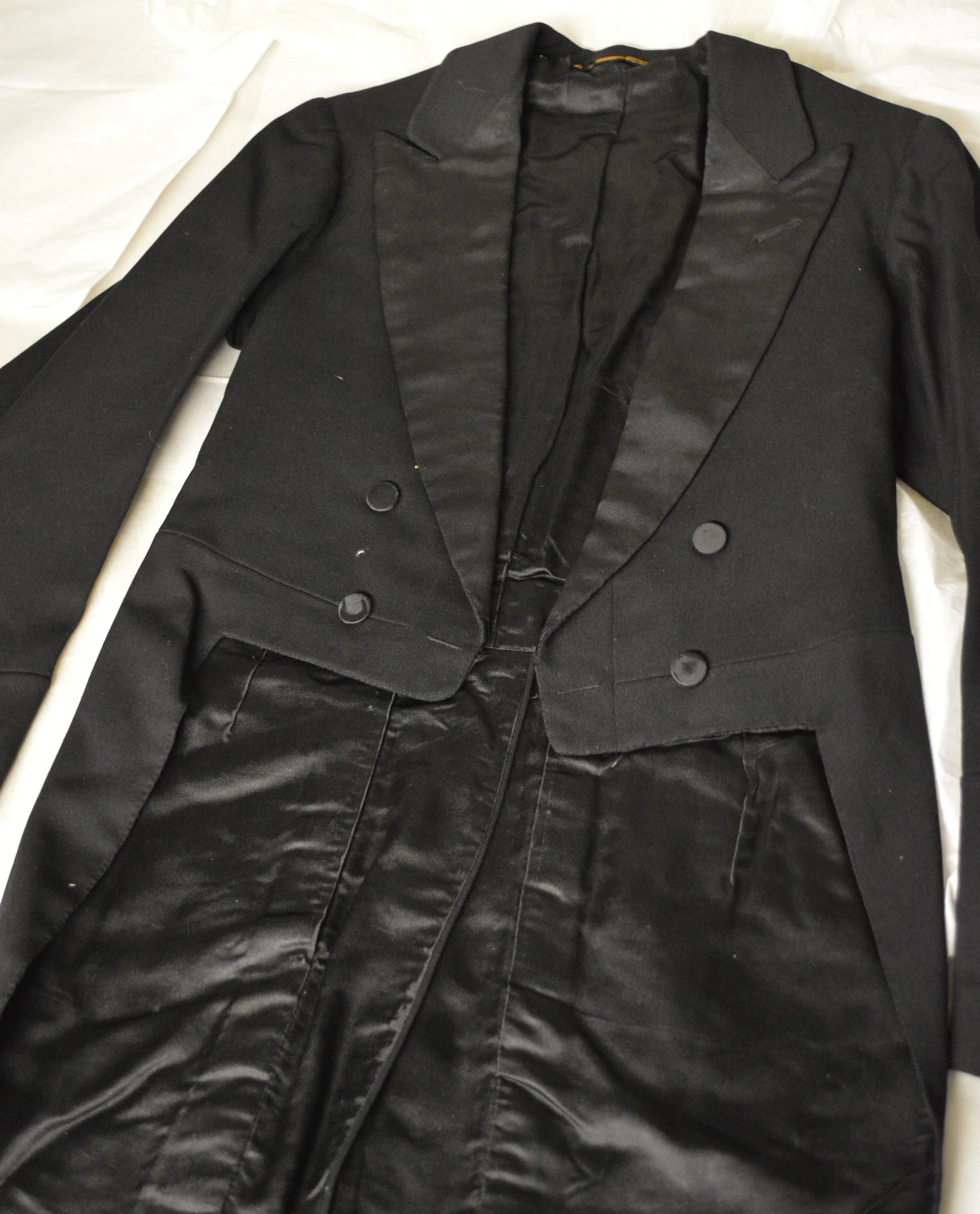 The black wool tailcoat from the Black Creek museum is laid flat on white archival paper.