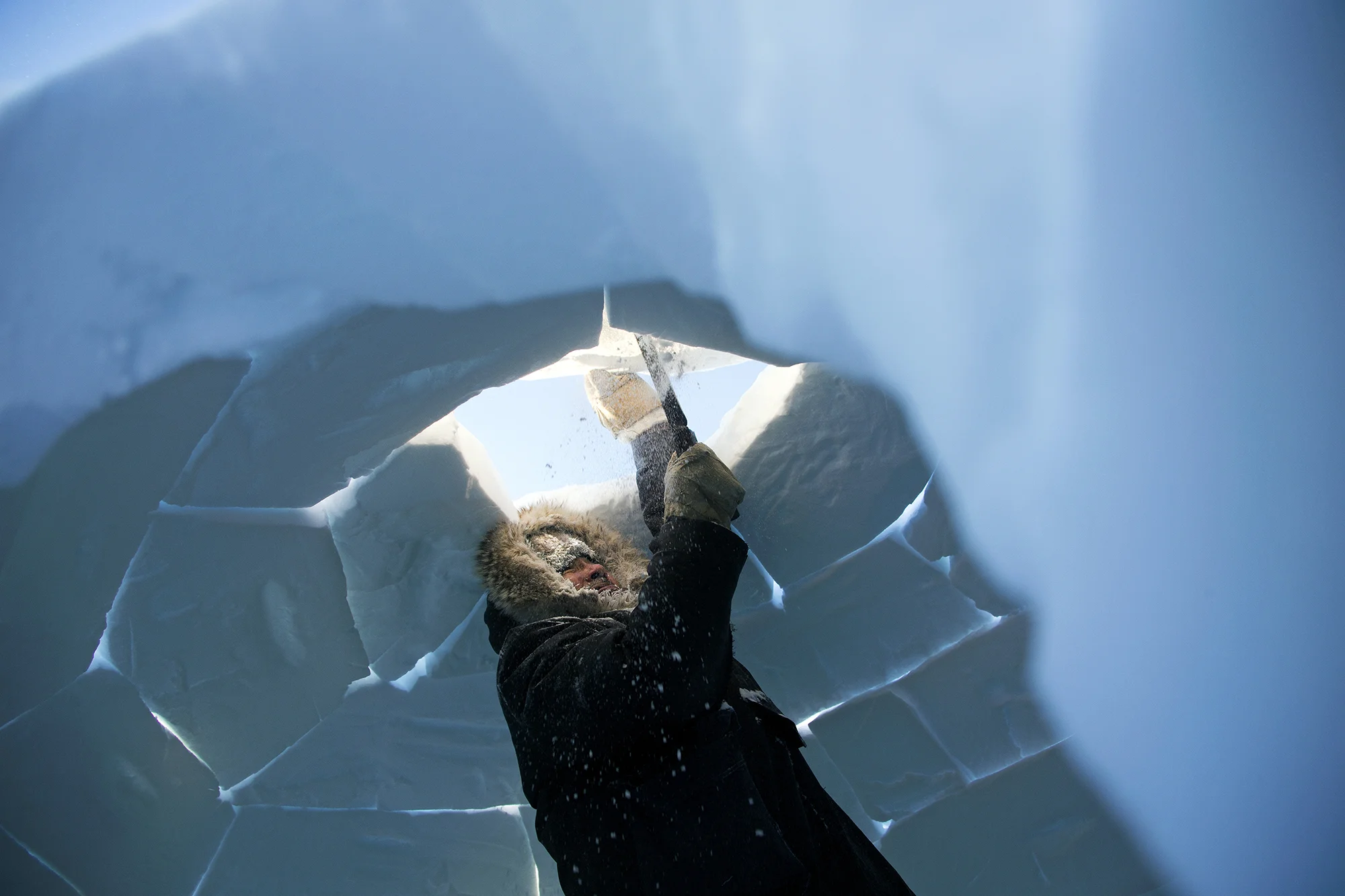 An Inuit elder placed the final block on an igloo he made while on the land in the middle of winter. With outside temperatures at -55 degrees Celcius with windchill, igloos provide much needed warmth and help shield from powerful wind storms. A skilled igloo carver can make one in about an hour. Hall Beach, Nunavut, Canada. 