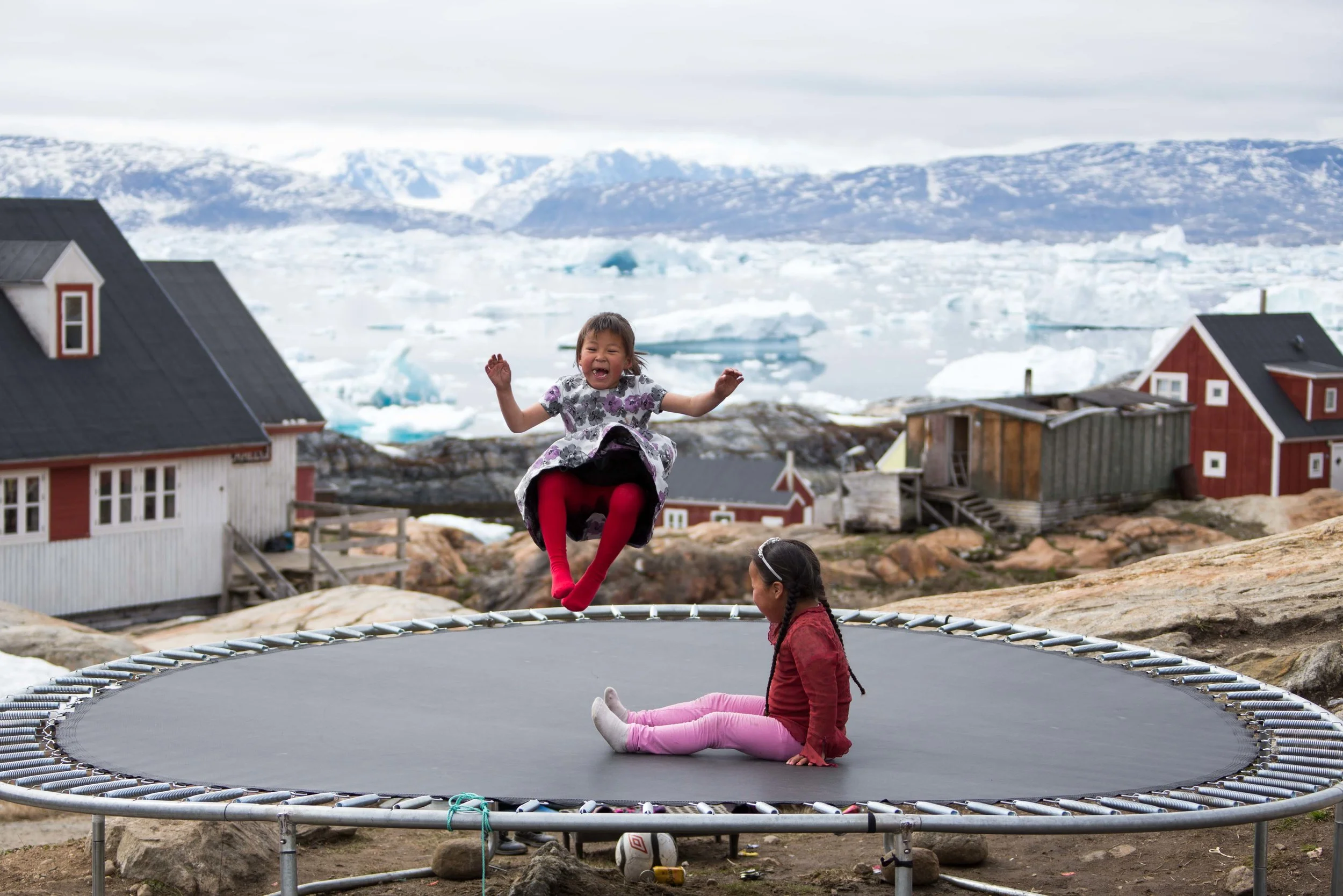 Two little girls bounce on a trampoline in Tinit, East Greenland. Photo: Matt Reichel. 