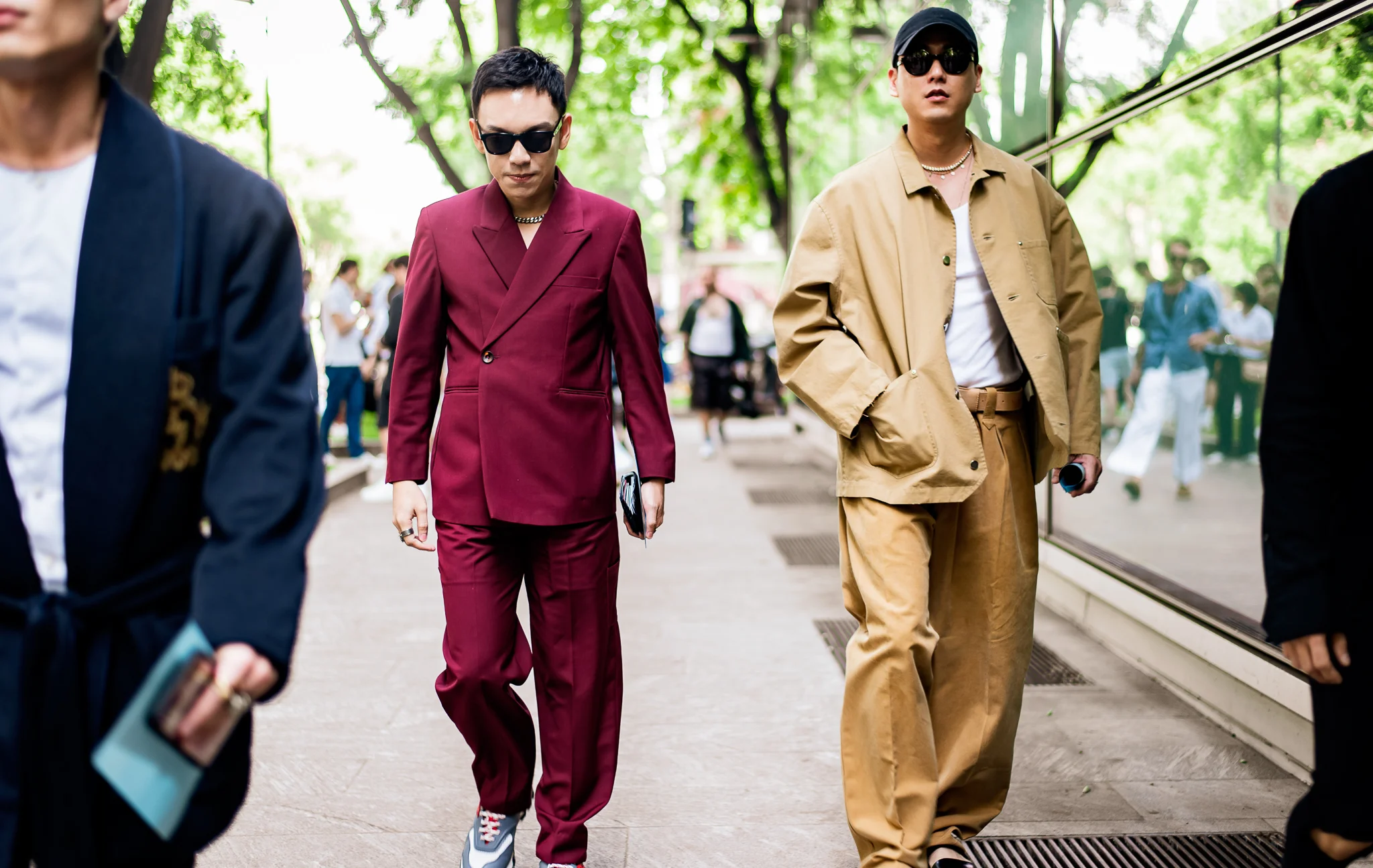 On the left, he’s wearing an imaginative version of a double-breasted suit (the one-button blazer, the chain replacing the traditional shirt, and the sneakers). On the right, he’s wearing a street interpretation of work-wear (specified by the gold neck-wear, and baseball hat). Despite their differences, both outfits experiment, shifting away from its traditional foundations