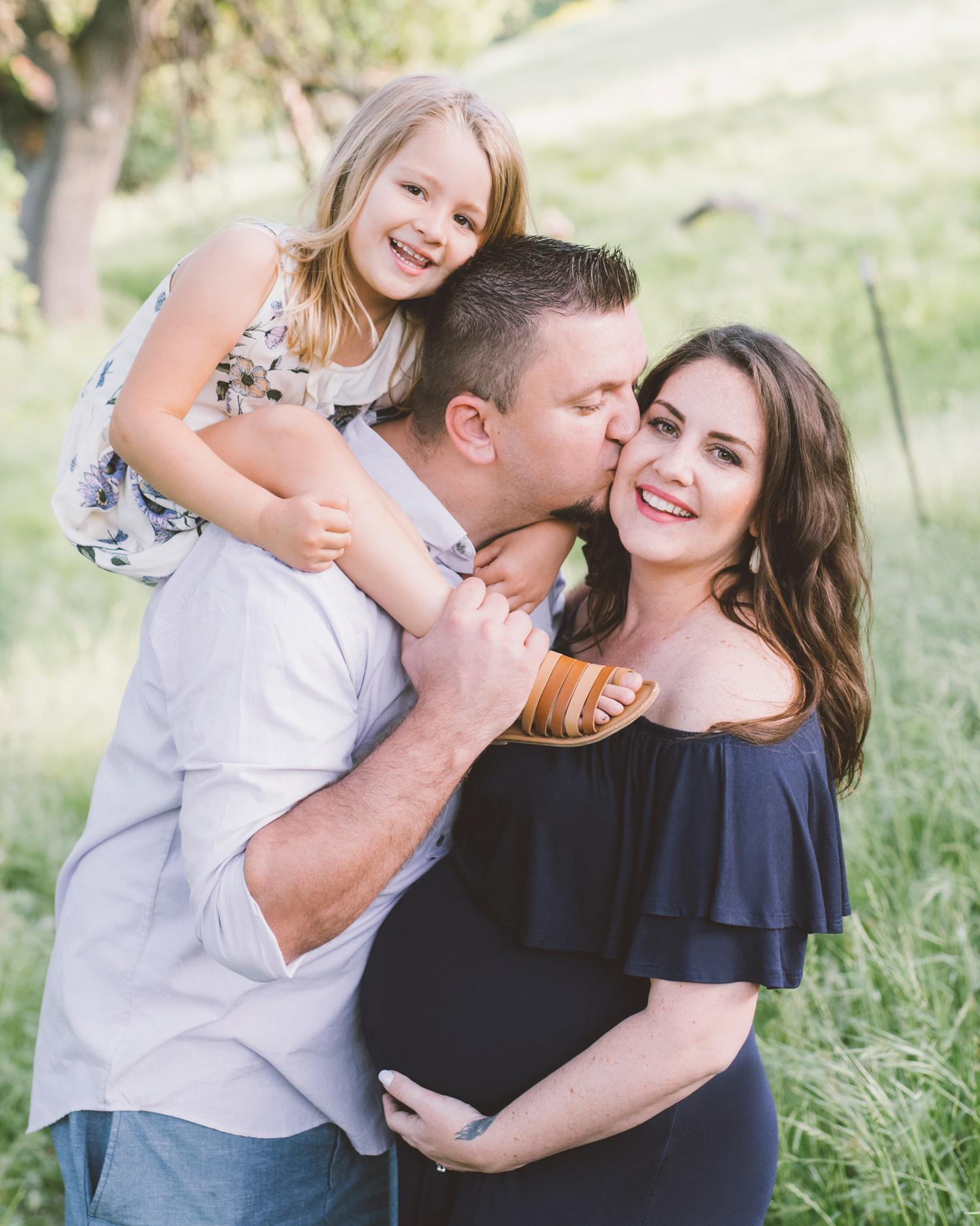 father-kissing-his-pregnant-wife-with-daughter-on-shoulders.jpg