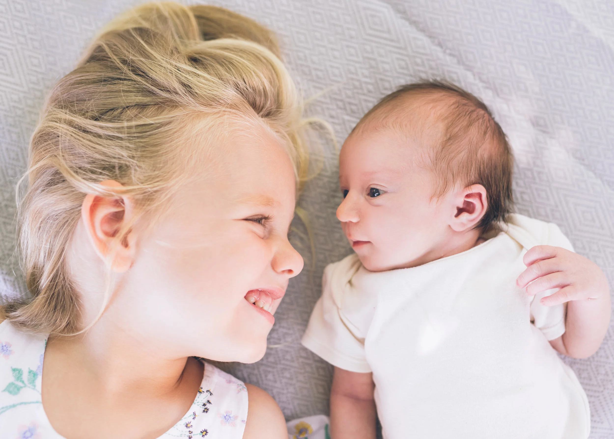 two-sisters-together-looking-at-each-other-during-lifestyle-newborn-portrait-session.jpg