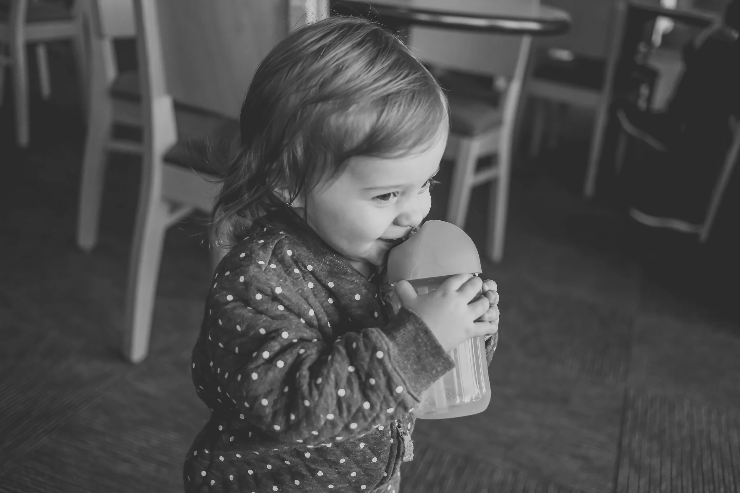 Toddler girl drinking from her cup at Panera Bread in Staten Island, NY. Documentary family photography.
