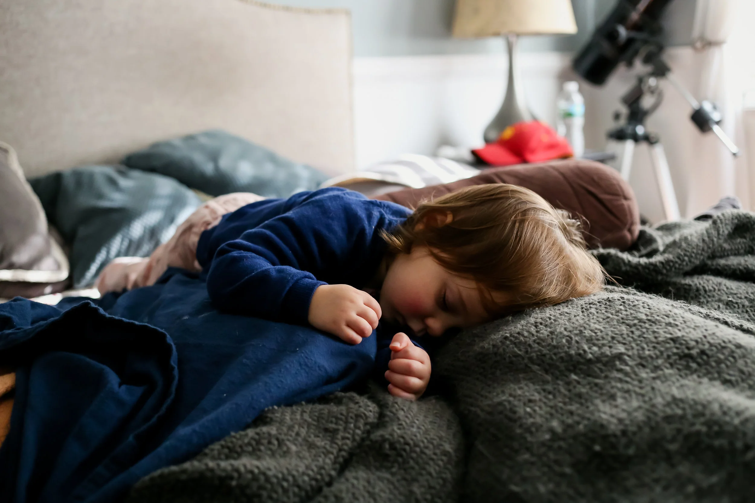 Two year old girl taking a nap on mom and dad's bed. At home candid family photography in Allentown, PA.