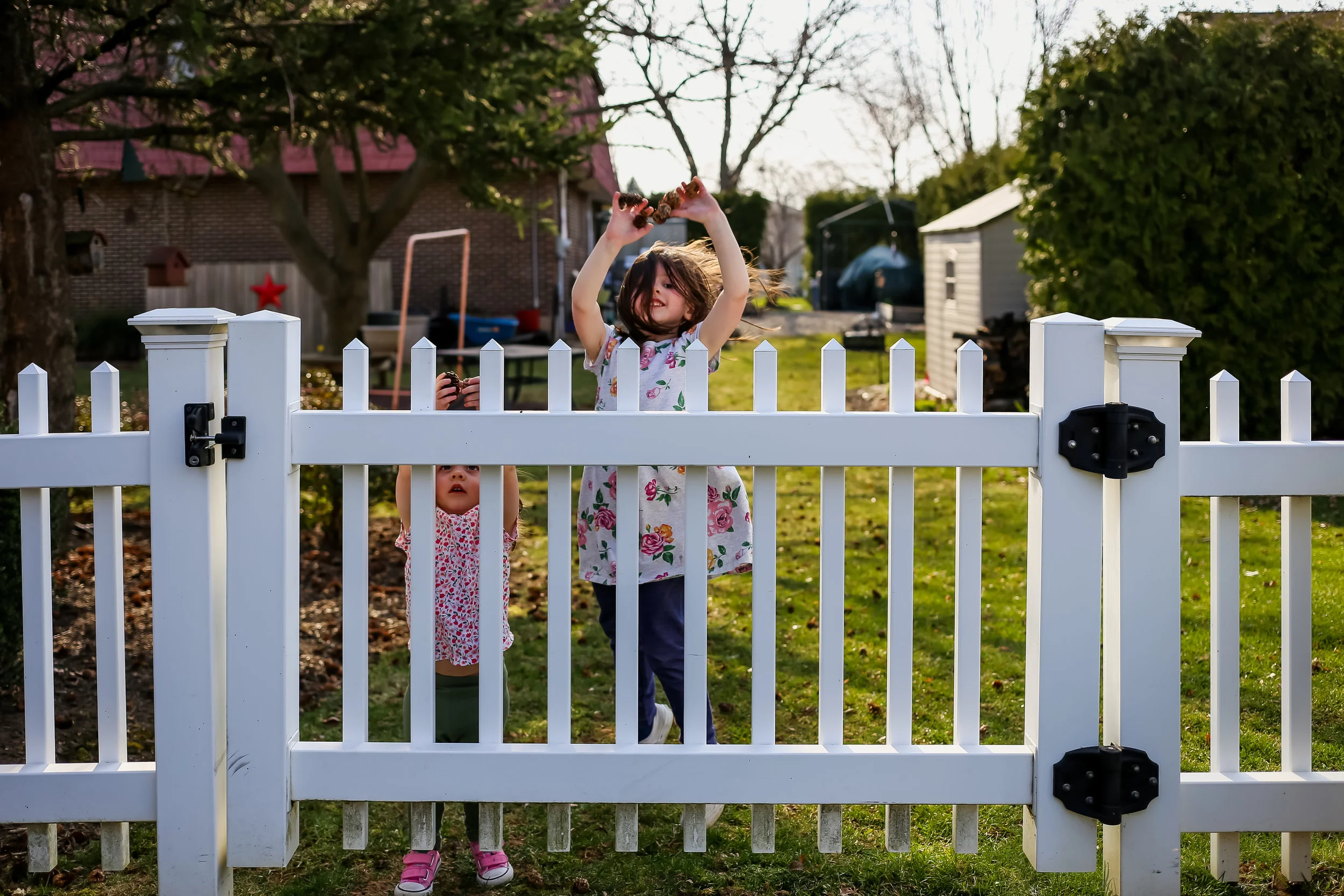 Little girls playing near behind a white picket fence in their backyard in Macungie, Pennsylvania.