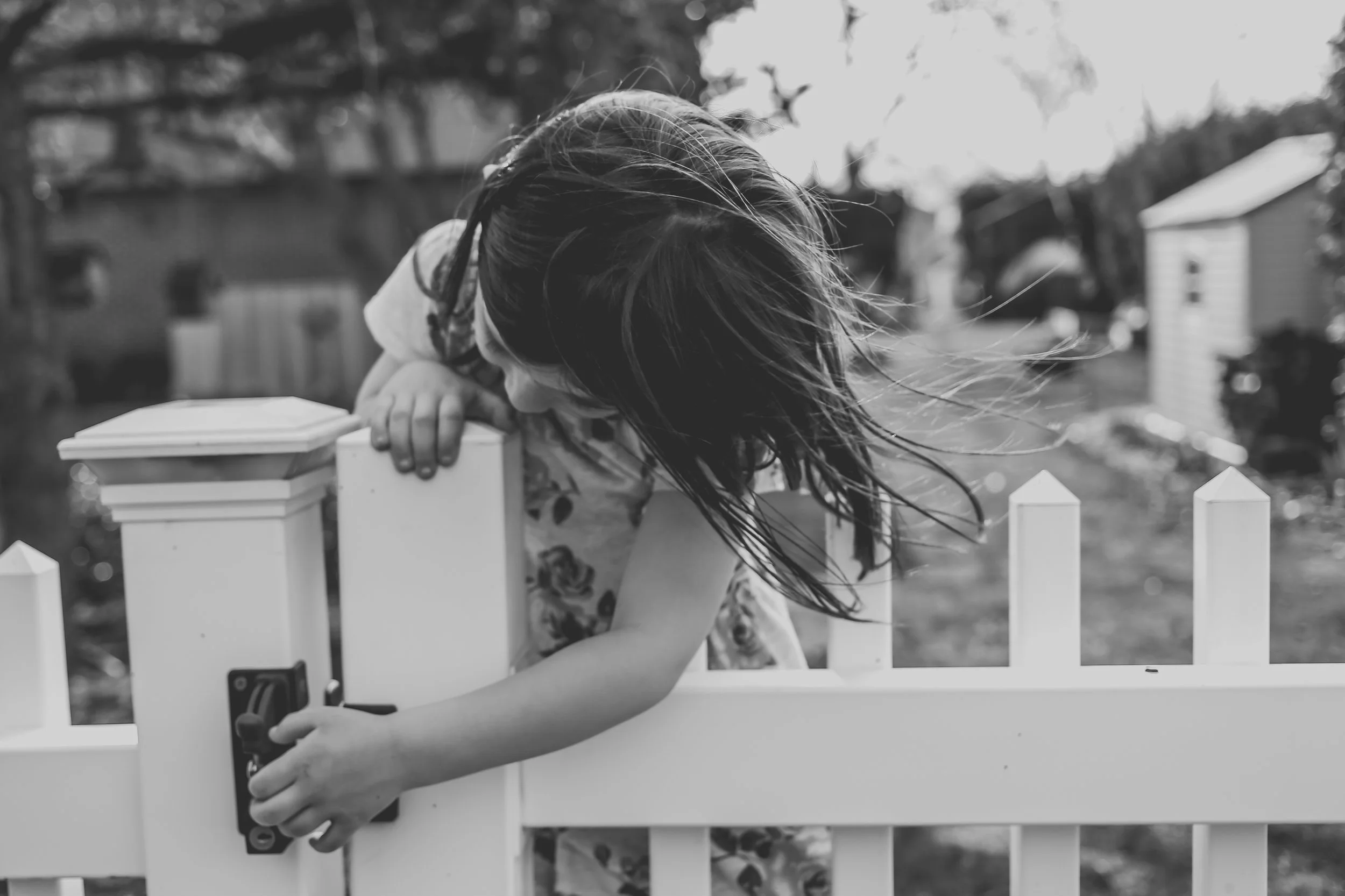 Girl trying to open the gate of a white picket fence on a warm spring day in Pennsylvania.