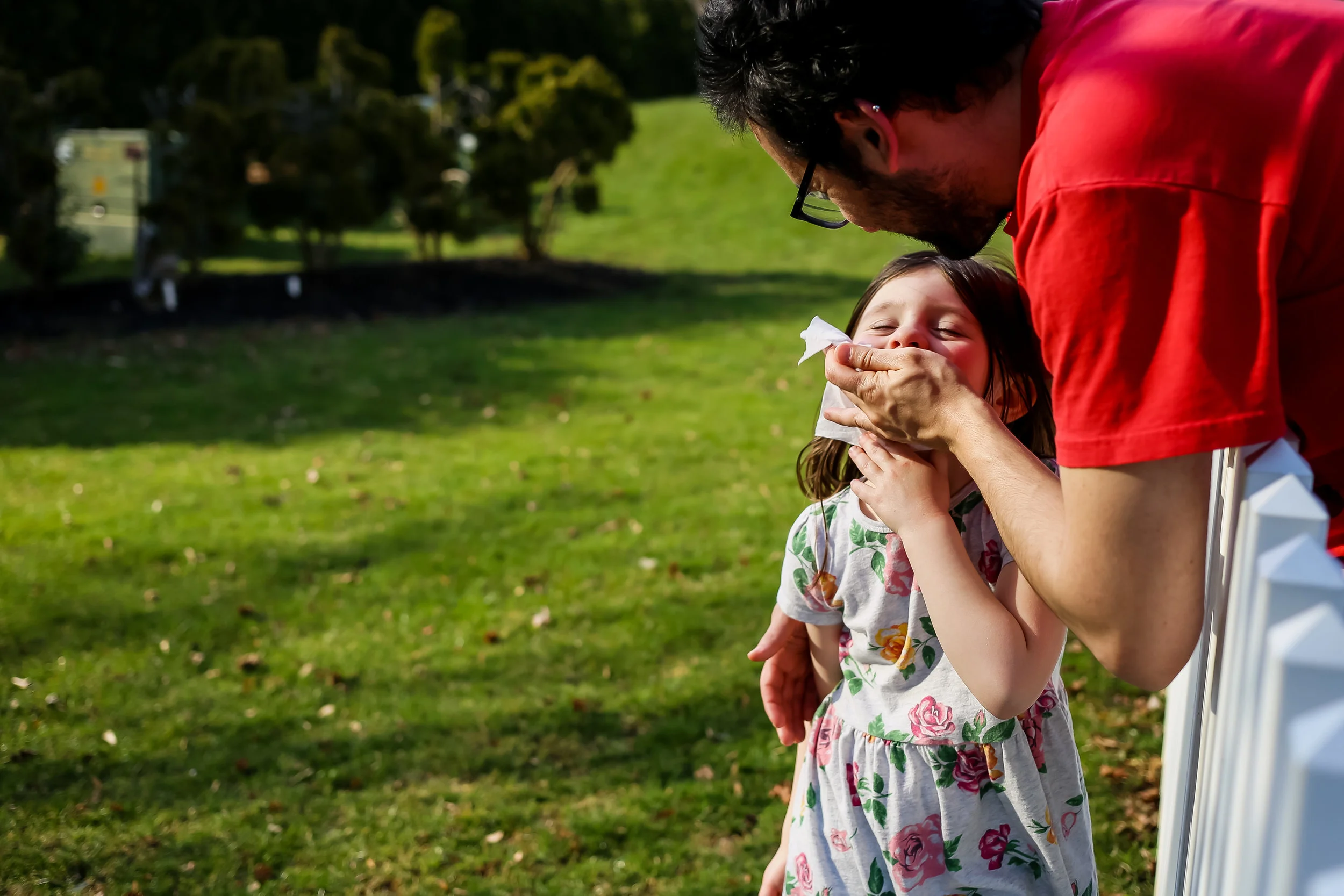 Father wiping his daughter's face while she plays outside in the backyard.