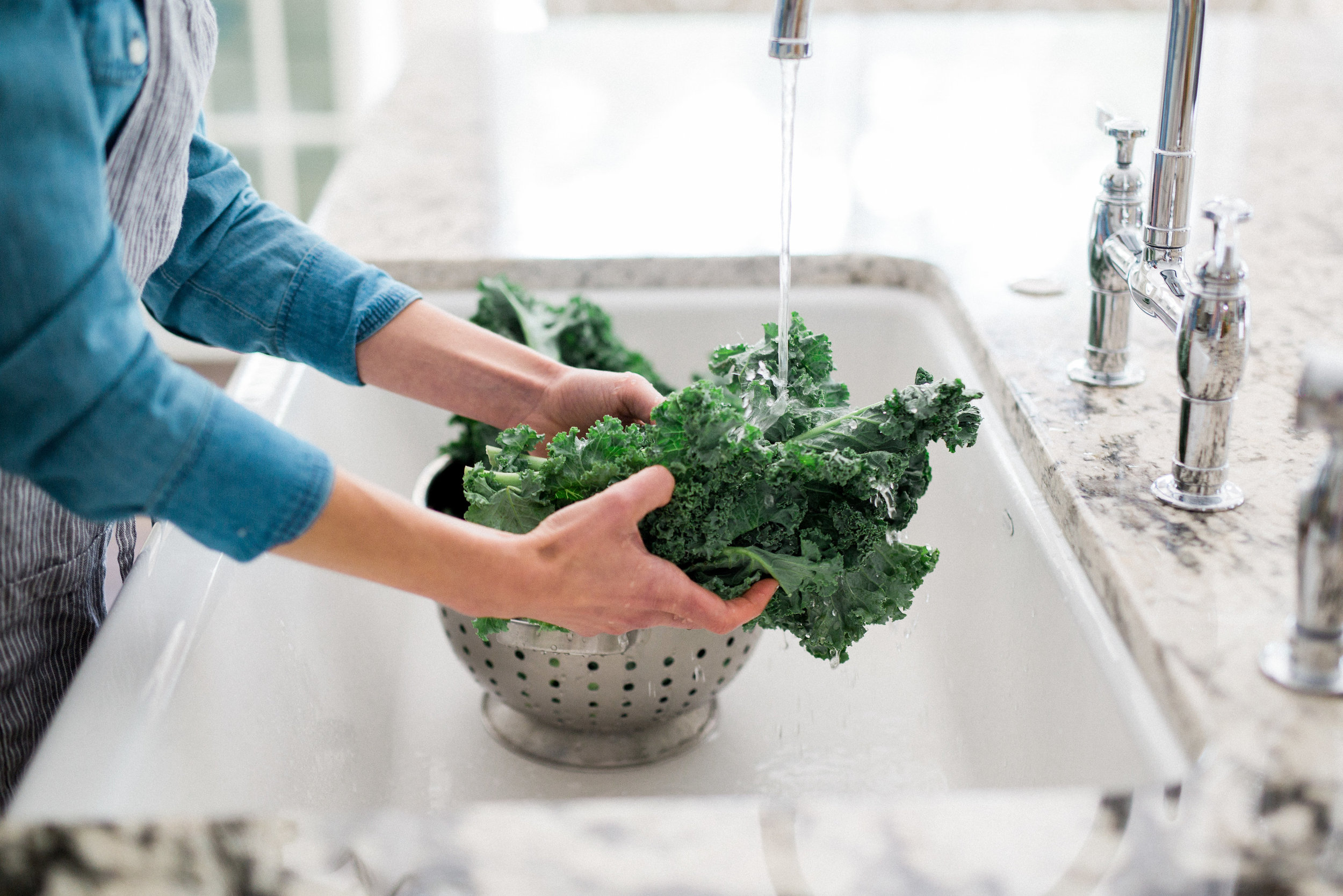 woman washing organic kale in stylish white kitchen