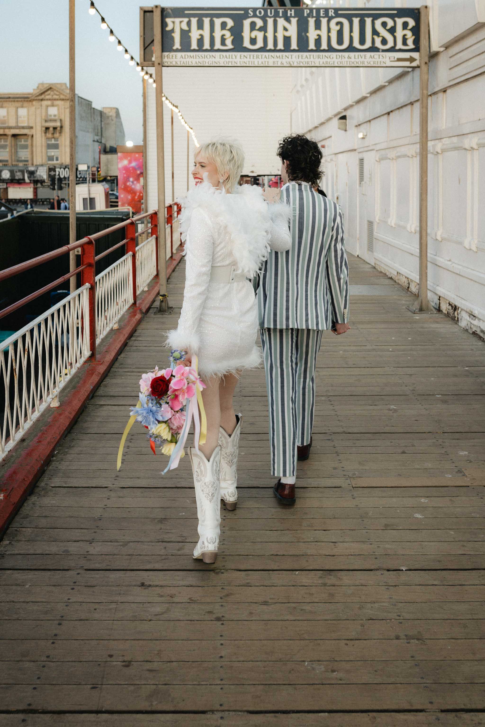 Couple walking away from camera in Blackpool pier in wedding outfits