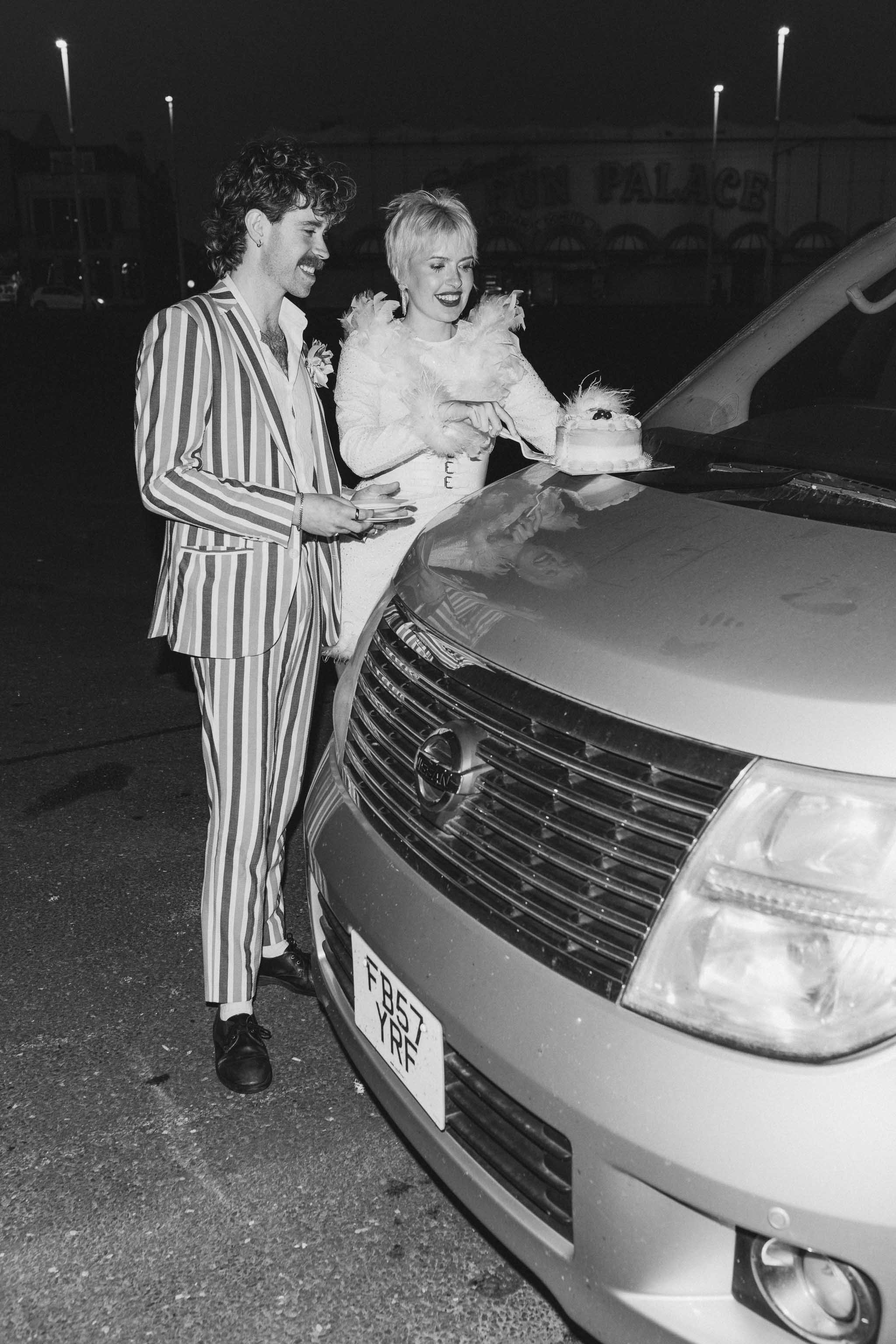 Couple eating vintage-inspired wedding cake on the hood of their camper van