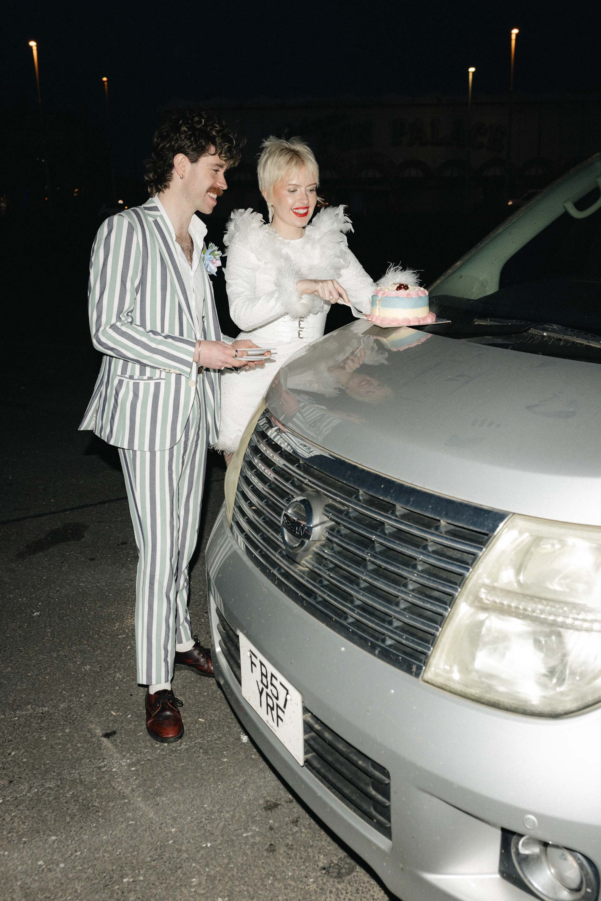 Couple eating vintage-inspired wedding cake on the hood of their camper van